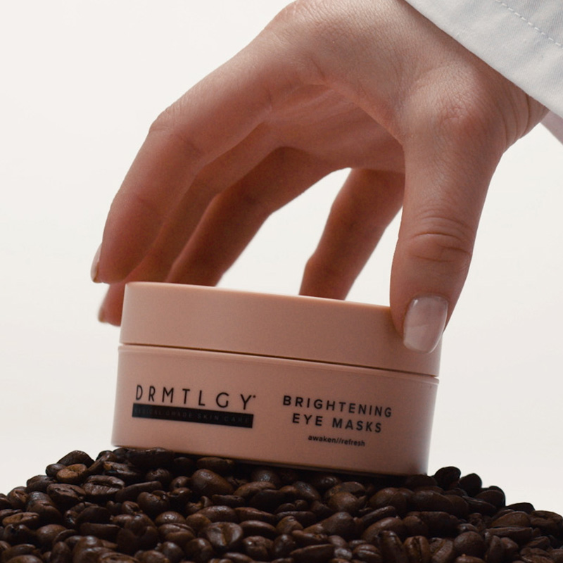 Hand holding a jar of brightening eye masks on coffee beans.