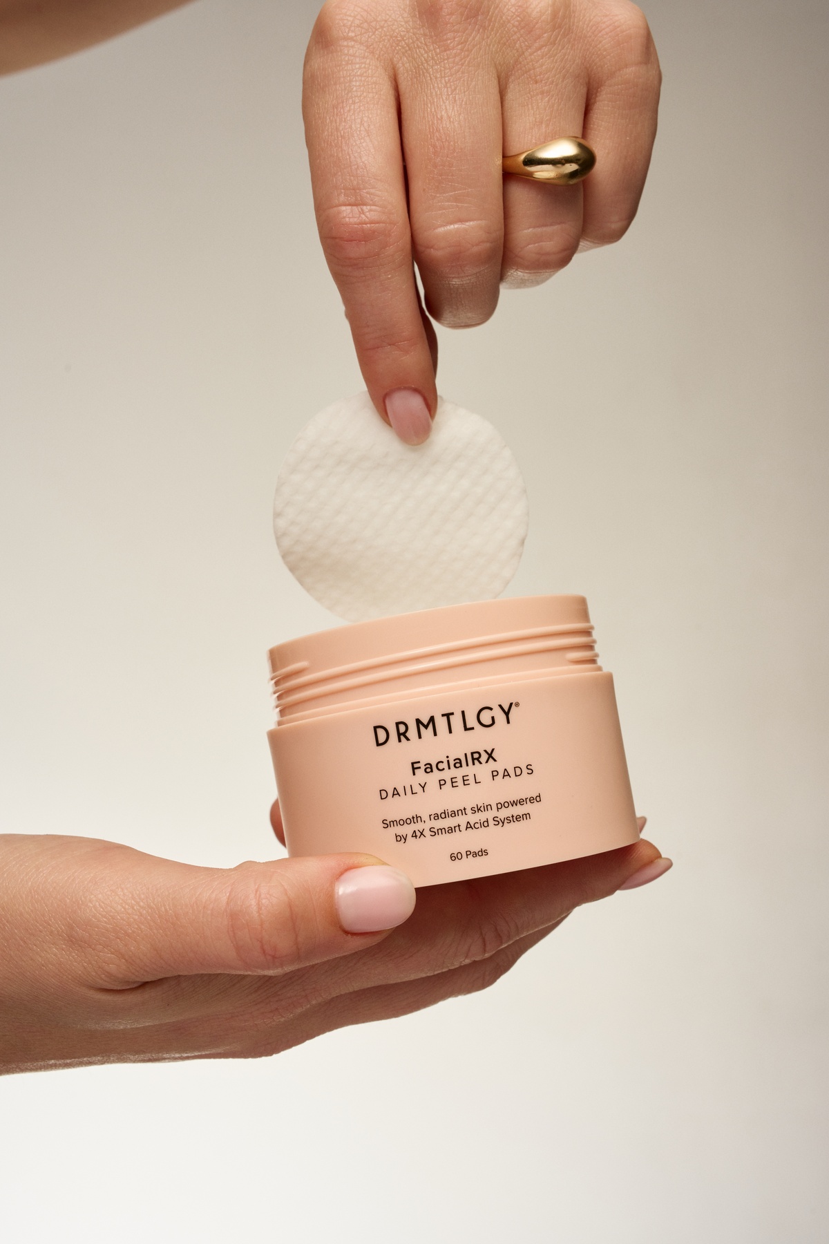 A person's hands holding a jar of DRMTLGY Daily Peel Pads, lifting one out.