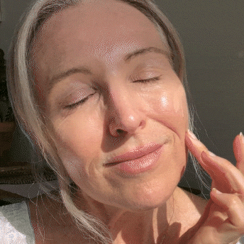 Person with closed eyes, smiling, touching face in sunlight.