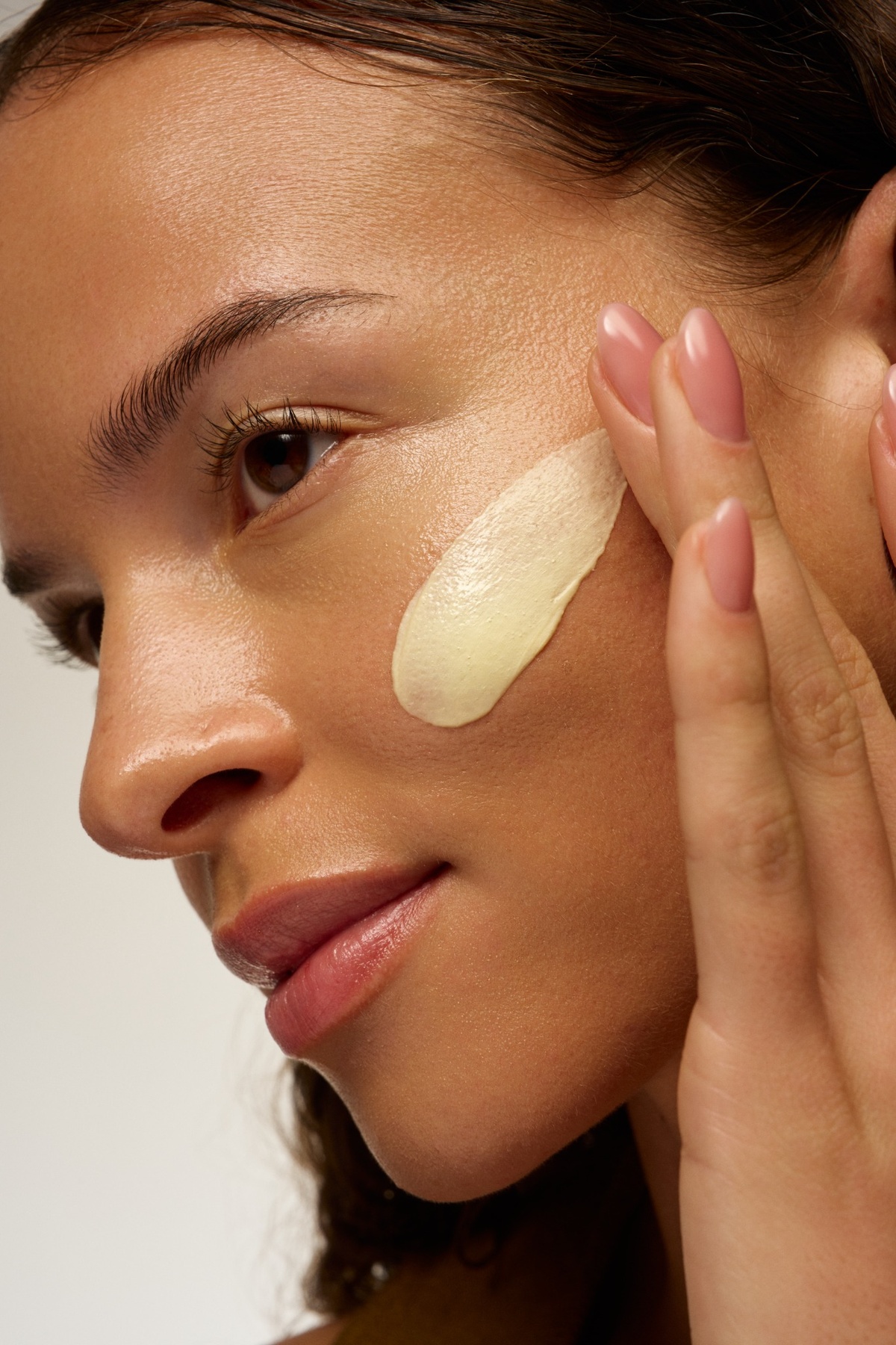 A close-up of a woman applying a swipe of cream to her cheek with her fingertips.