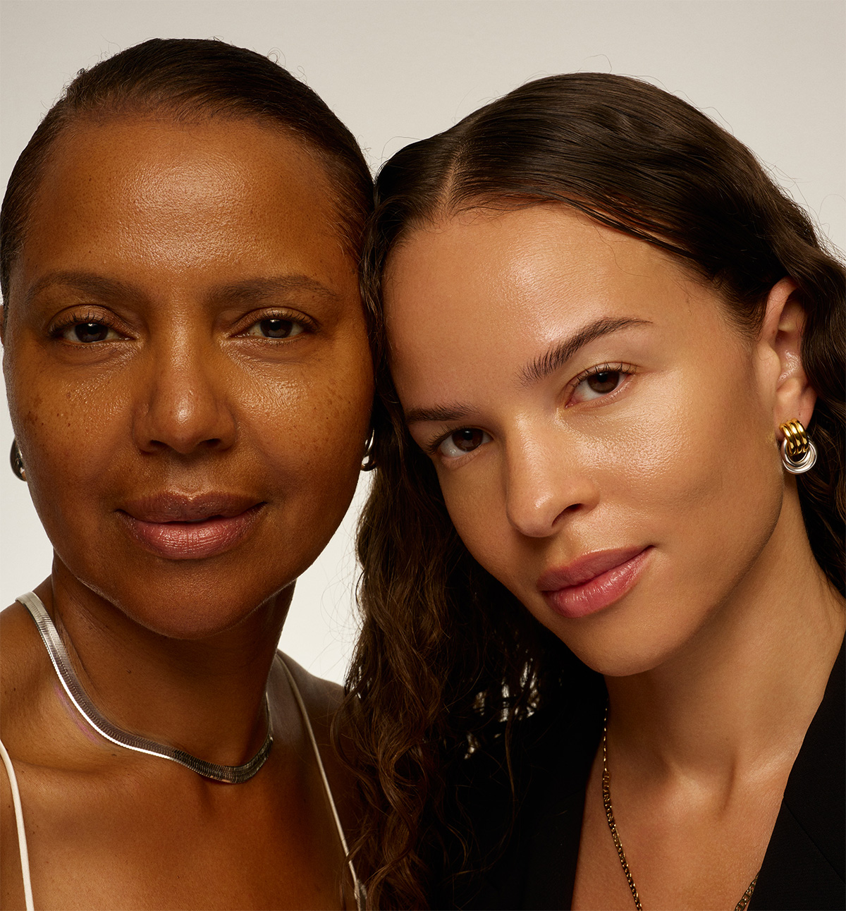 A close-up portrait of two women with different skin tones looking at the camera.