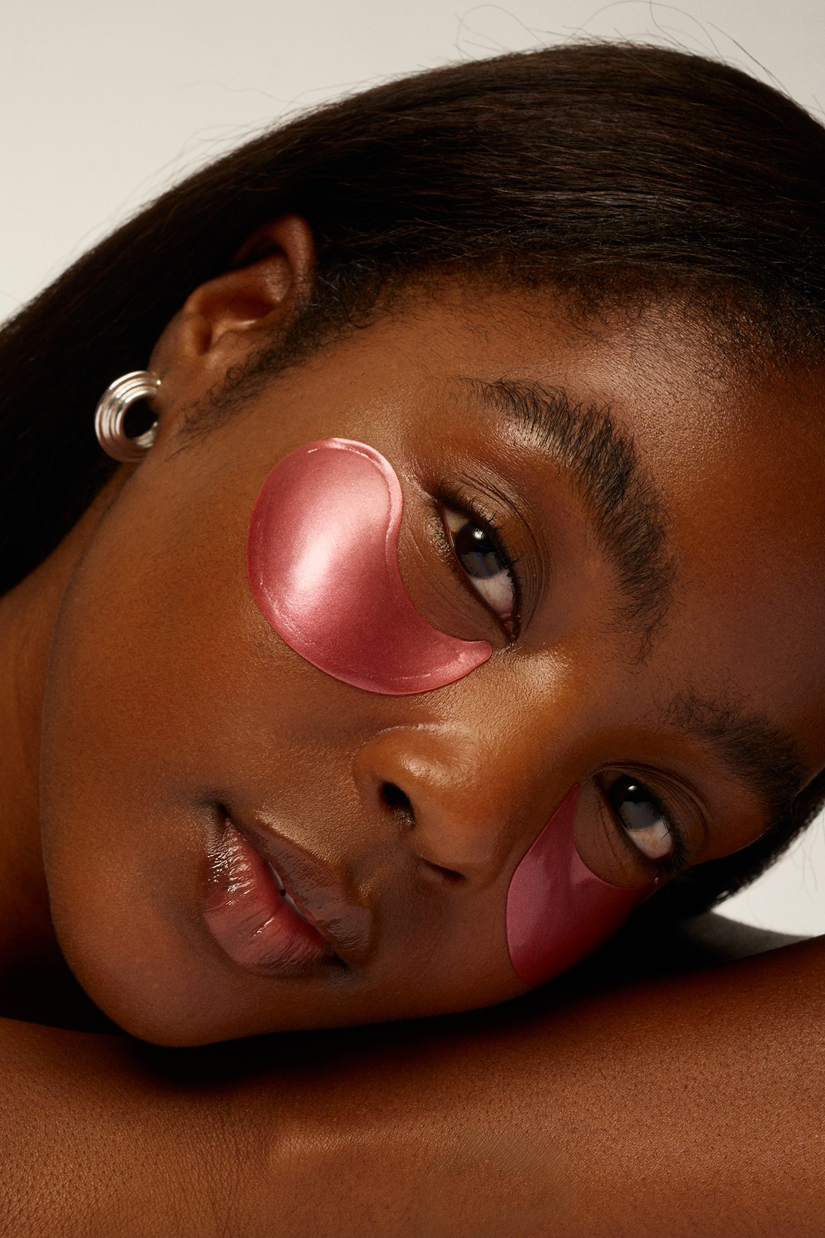 A close-up of a woman's face with shimmery pink hydrogel eye patches under her eyes.