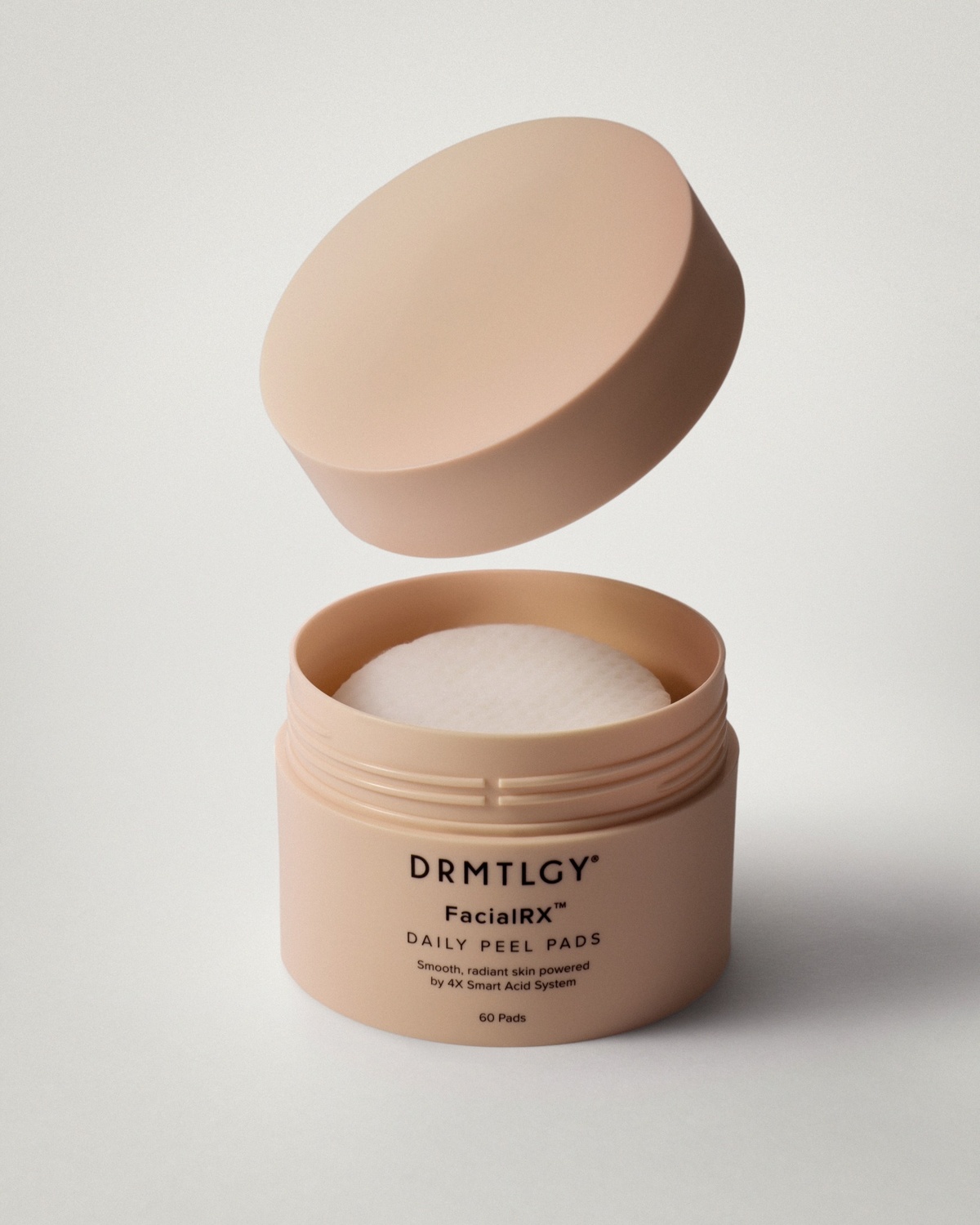 A light pink jar of DRMTLGY Daily Peel Pads is open, with the lid floating above it.