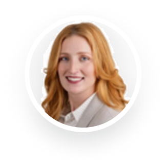 A circular headshot of a smiling woman with long, wavy reddish-blonde hair, wearing a blazer.