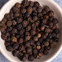 A bowl filled with whole black peppercorns.
