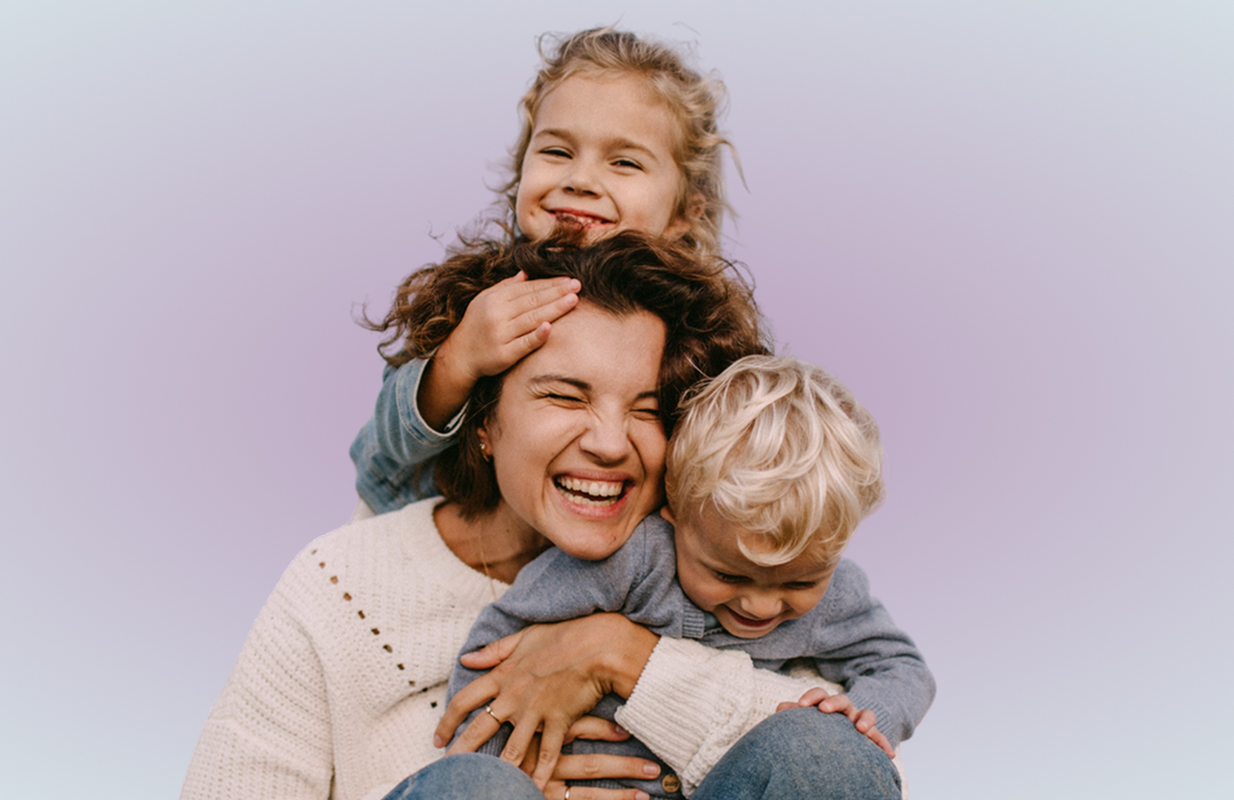 Smiling woman hugging two children against a purple background.