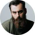 Man with a beard and serious expression, wearing a green shirt.
