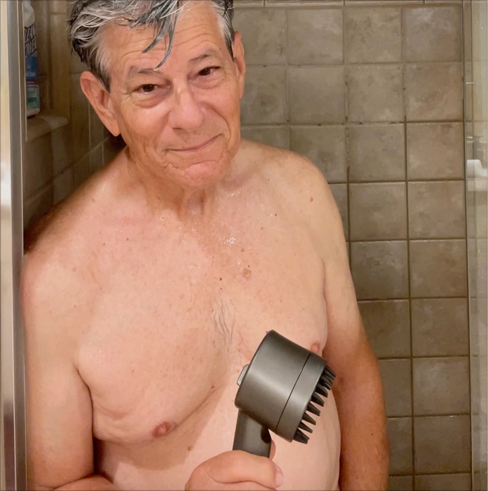 Man in a shower holding a gray handheld device.