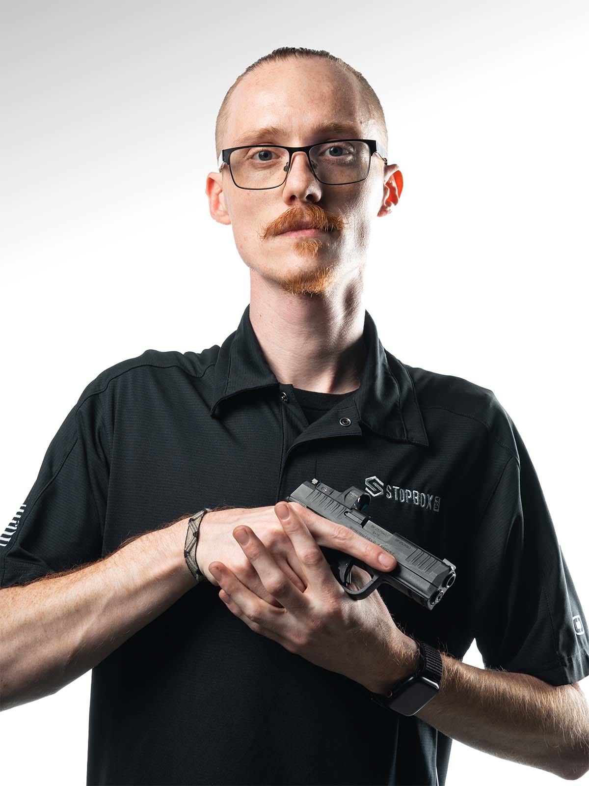 Person with glasses holding a handgun against a white background.