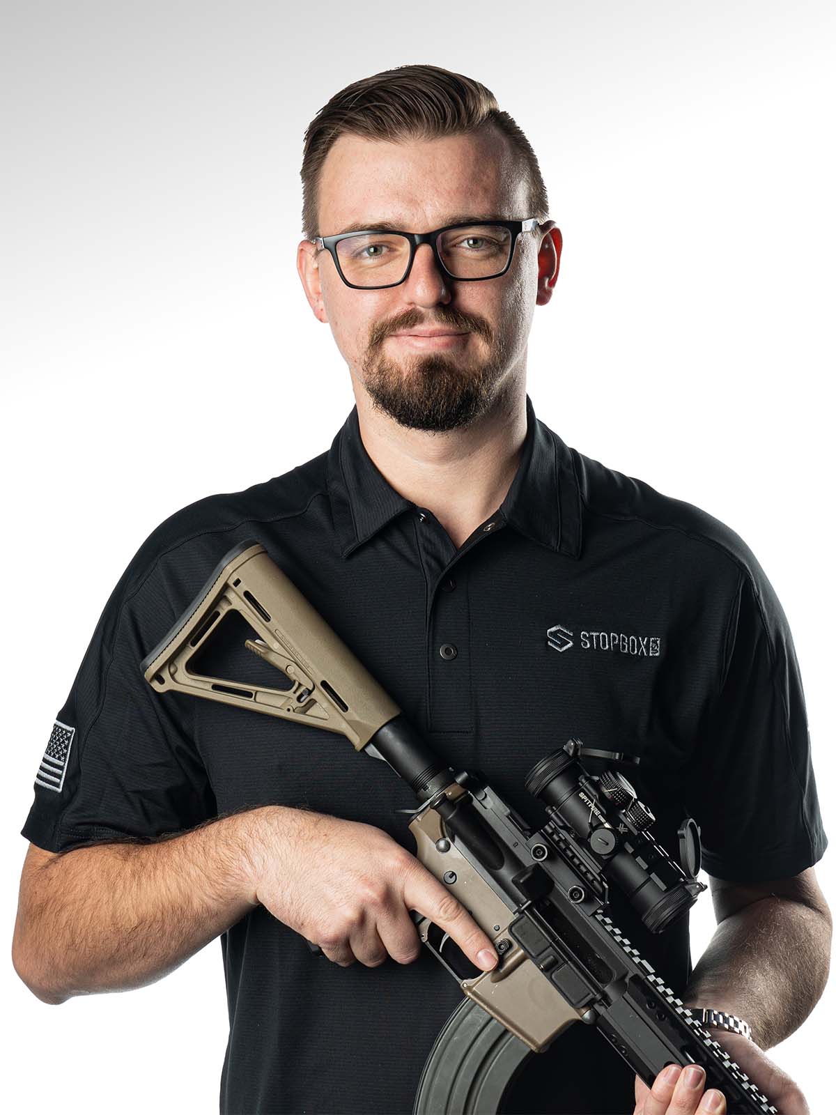 Person holding a rifle, wearing glasses and a black polo shirt.