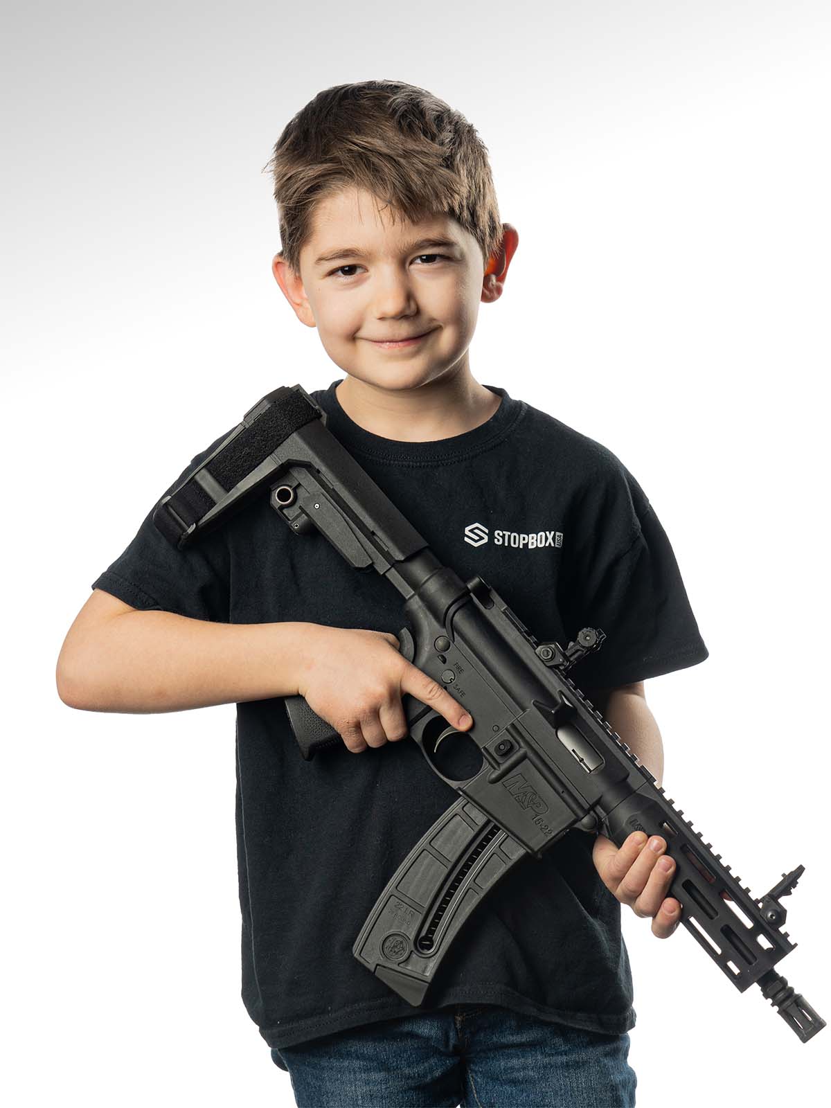 A young boy smiling, holding a rifle, on a white background.