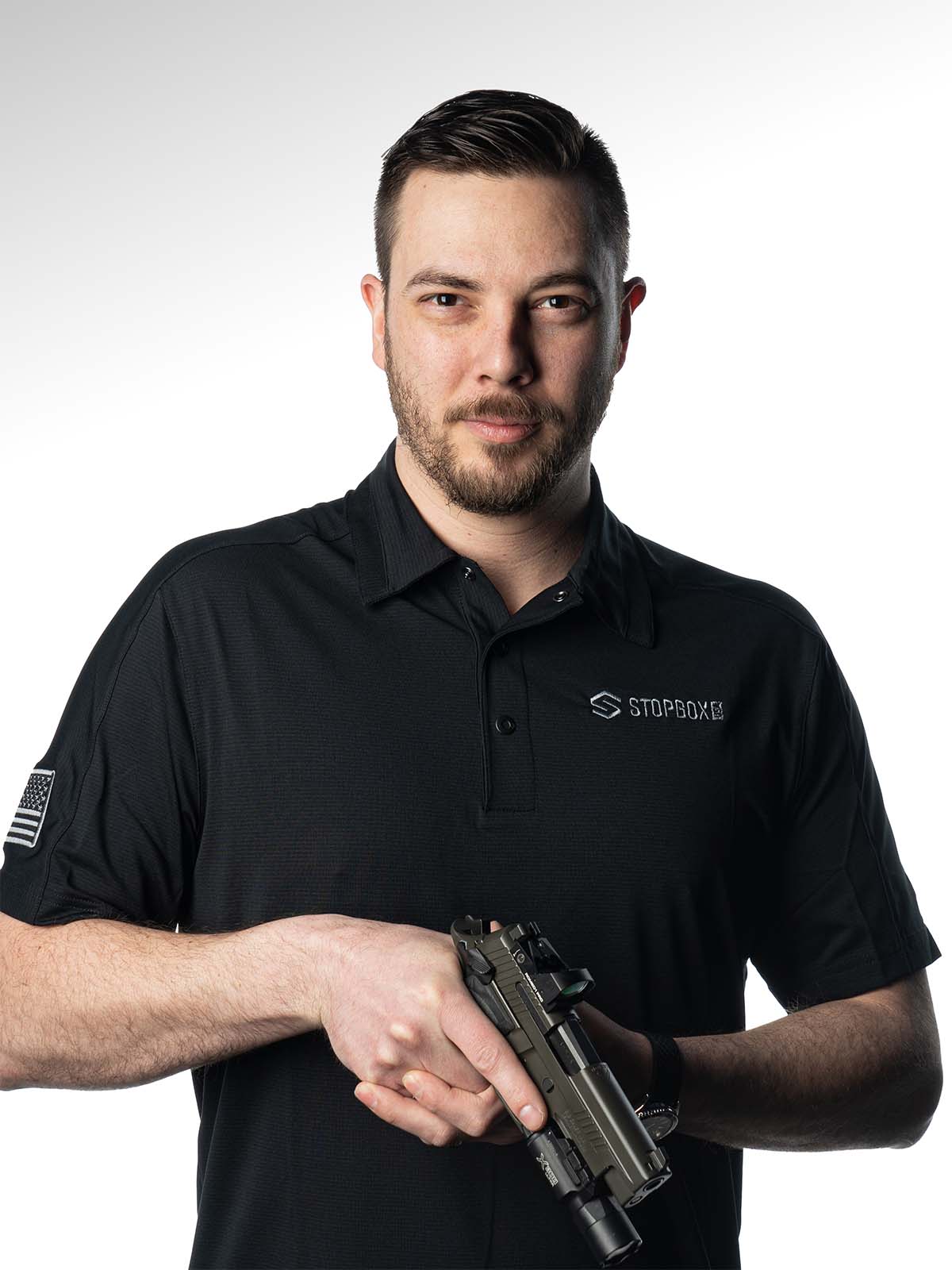 Man in a black shirt holding a firearm against a plain background.