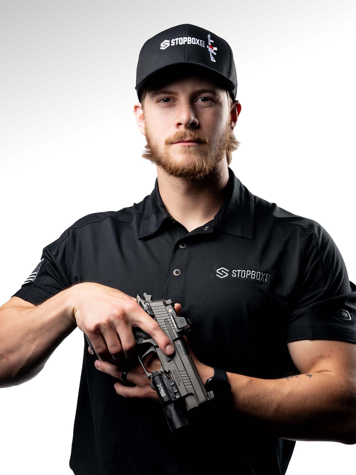 Person in black attire holding a firearm against a white background.