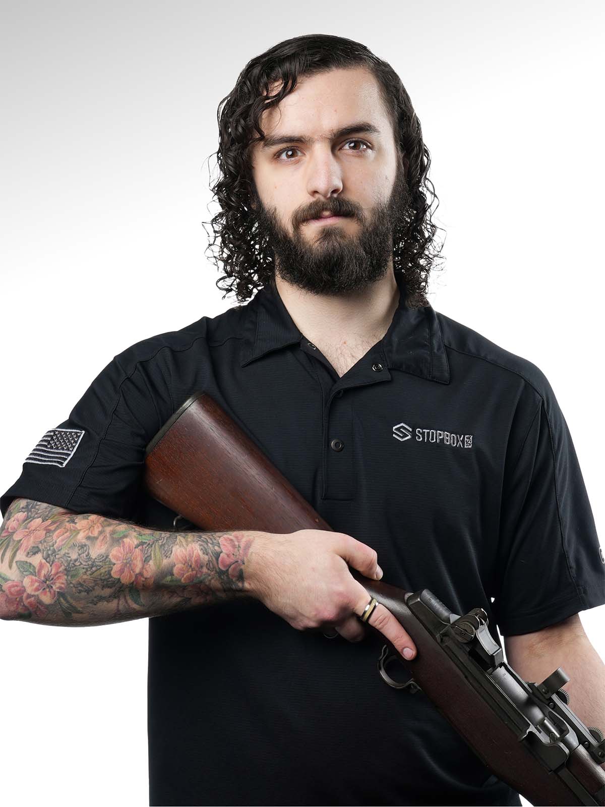 Person holding a rifle, wearing a black shirt with tattooed arm.