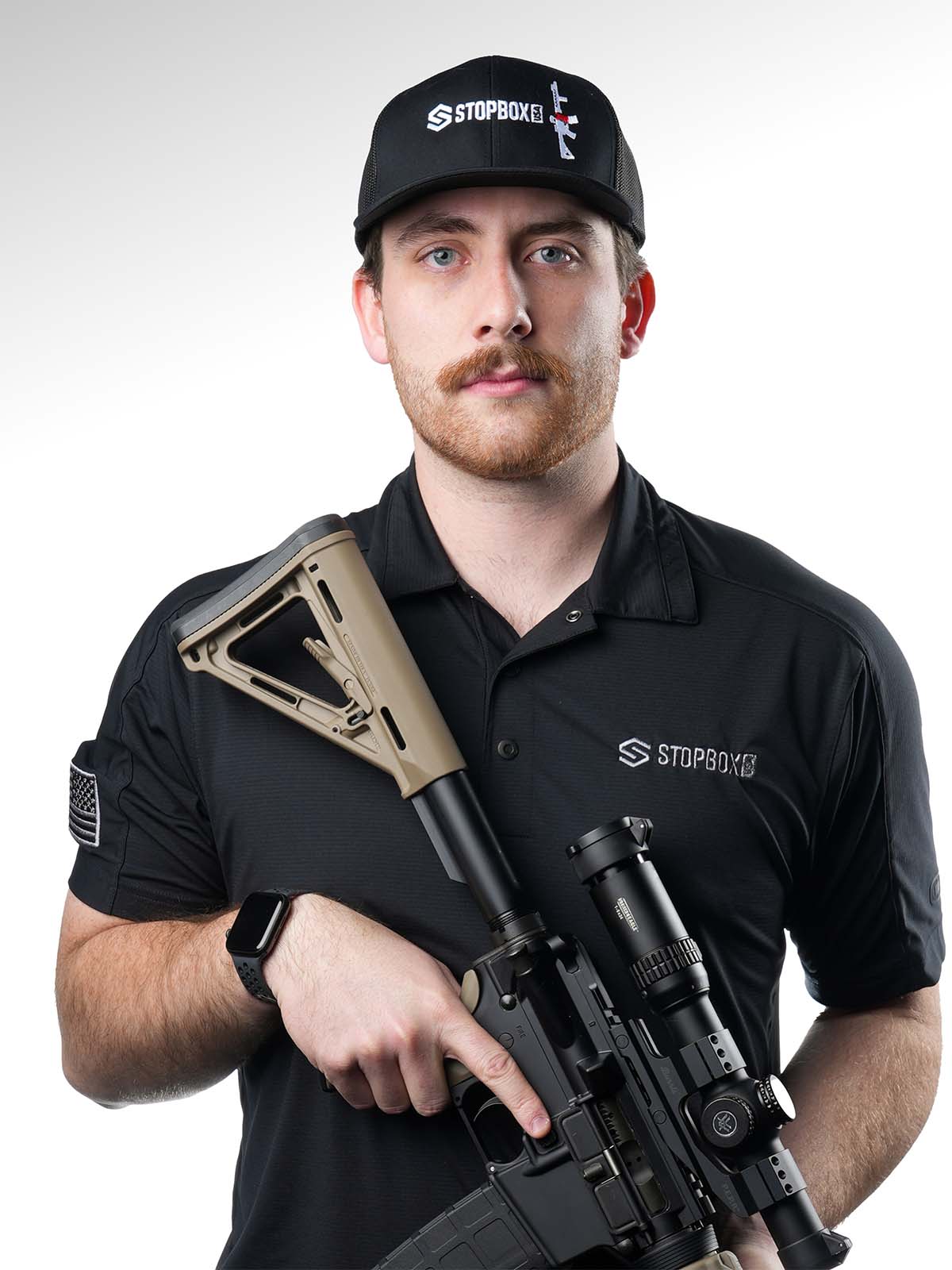 Person holding a rifle, wearing a black cap and polo with 'STOPBOX' logo.