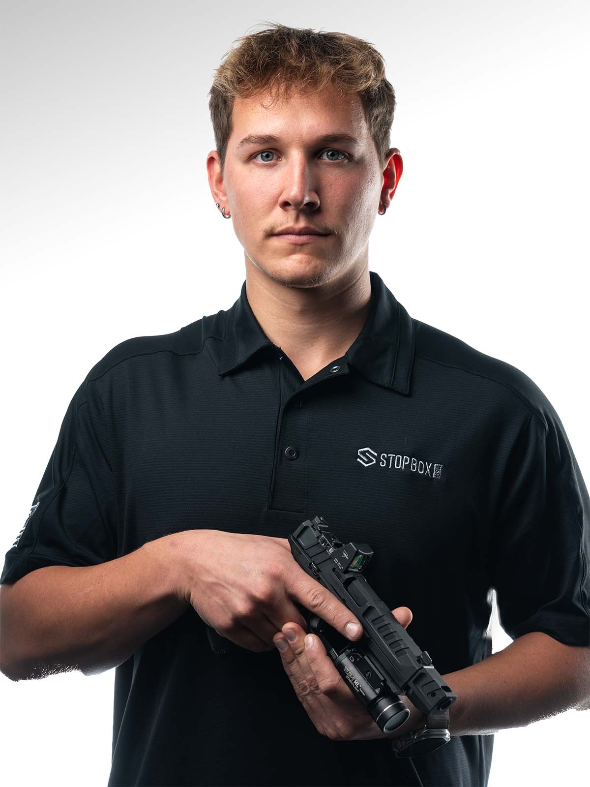 Person holding a firearm with a serious expression, wearing a black polo shirt.