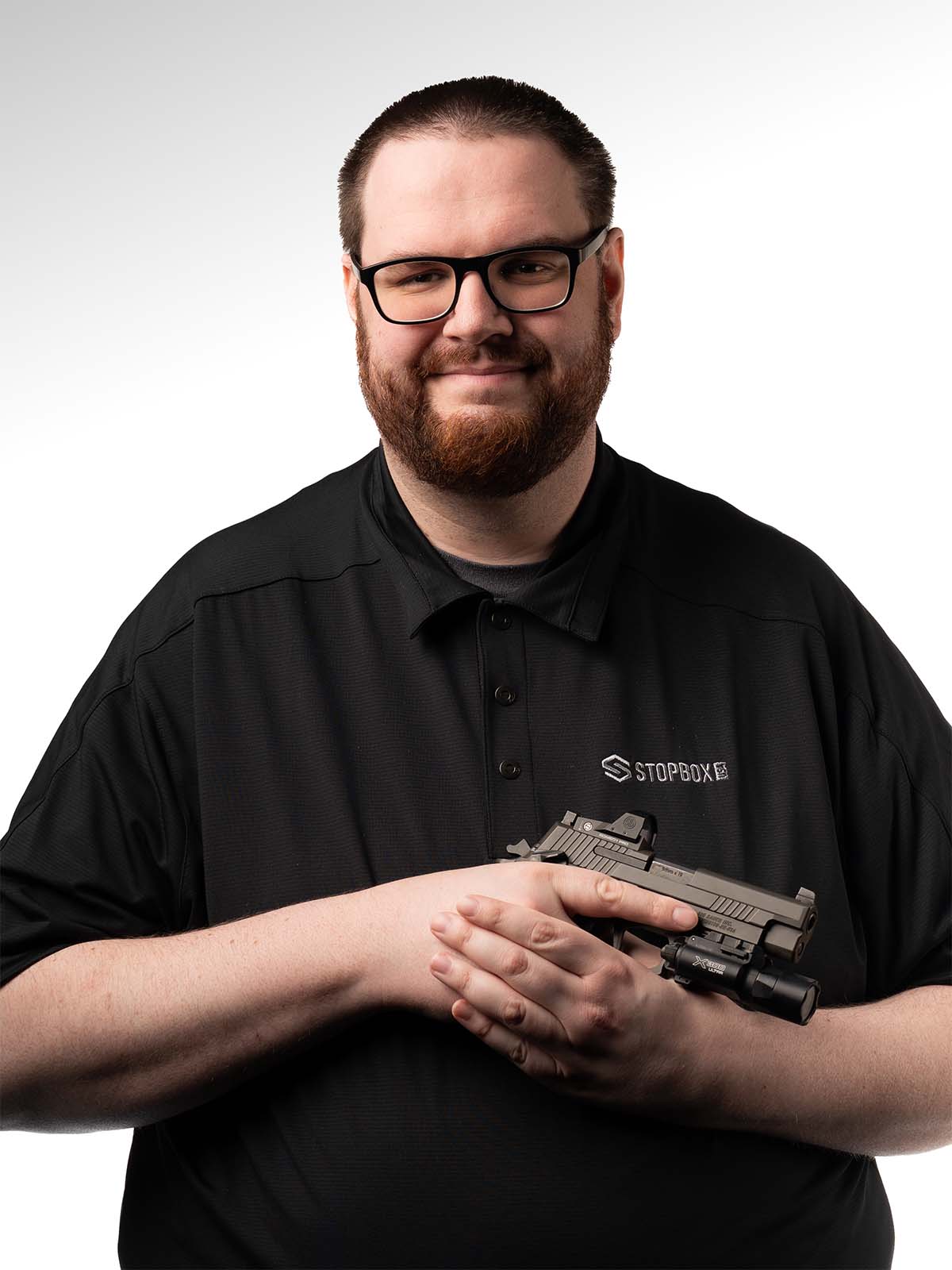 Person in black shirt holding a handgun against a white background.