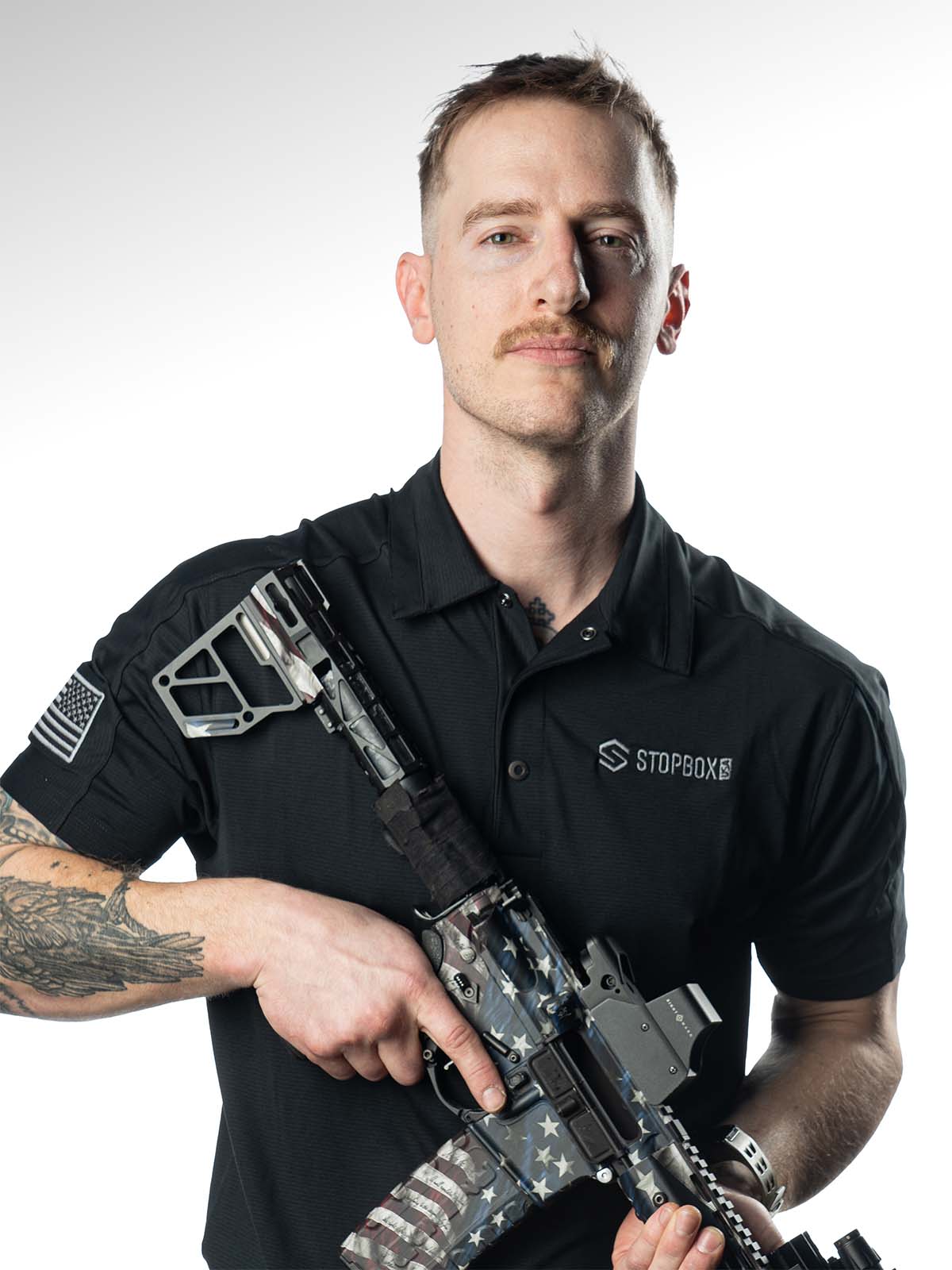 Person holding a painted rifle, wearing a black polo shirt.