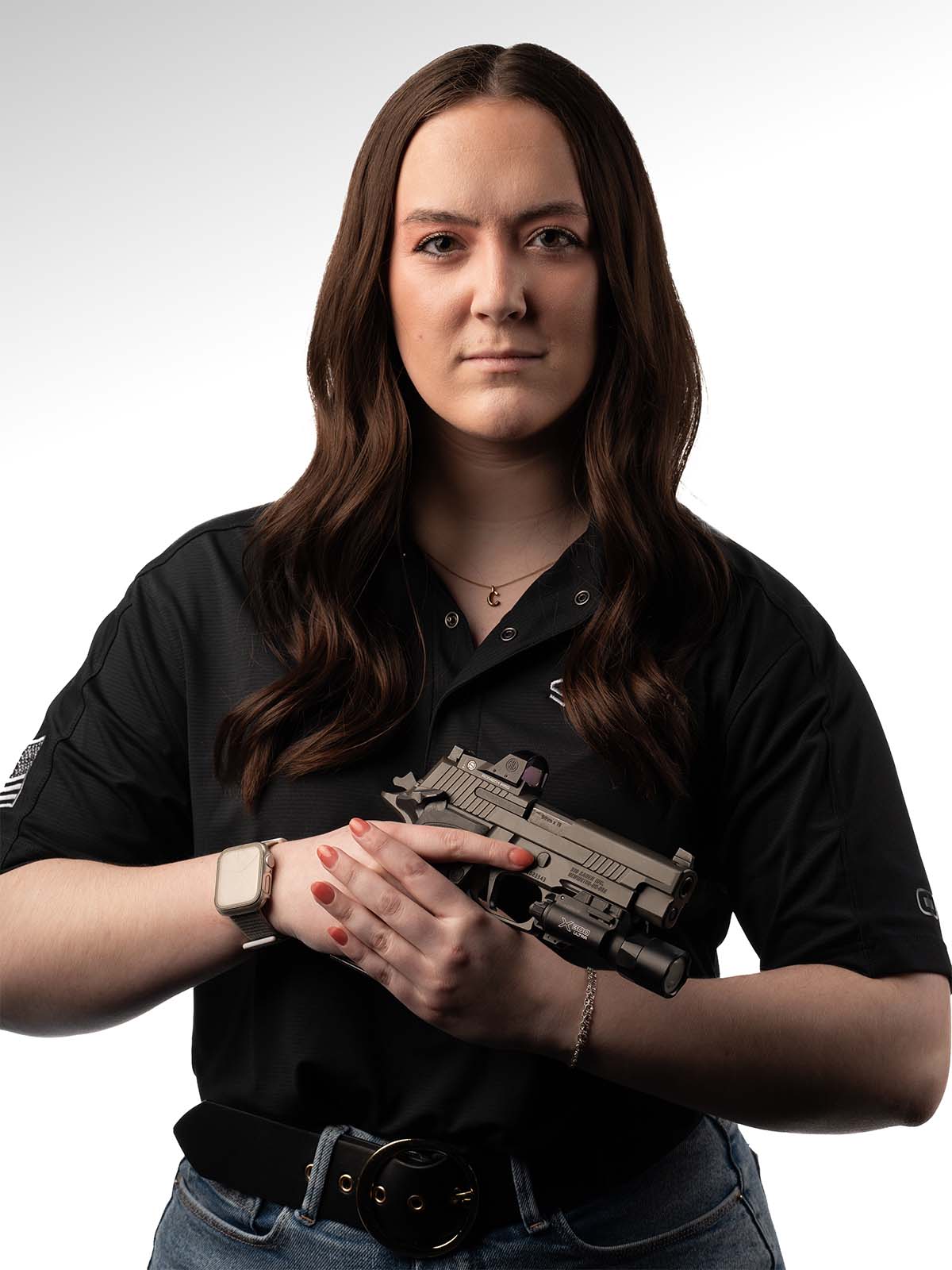 Person in a black shirt holding a firearm against a plain background.