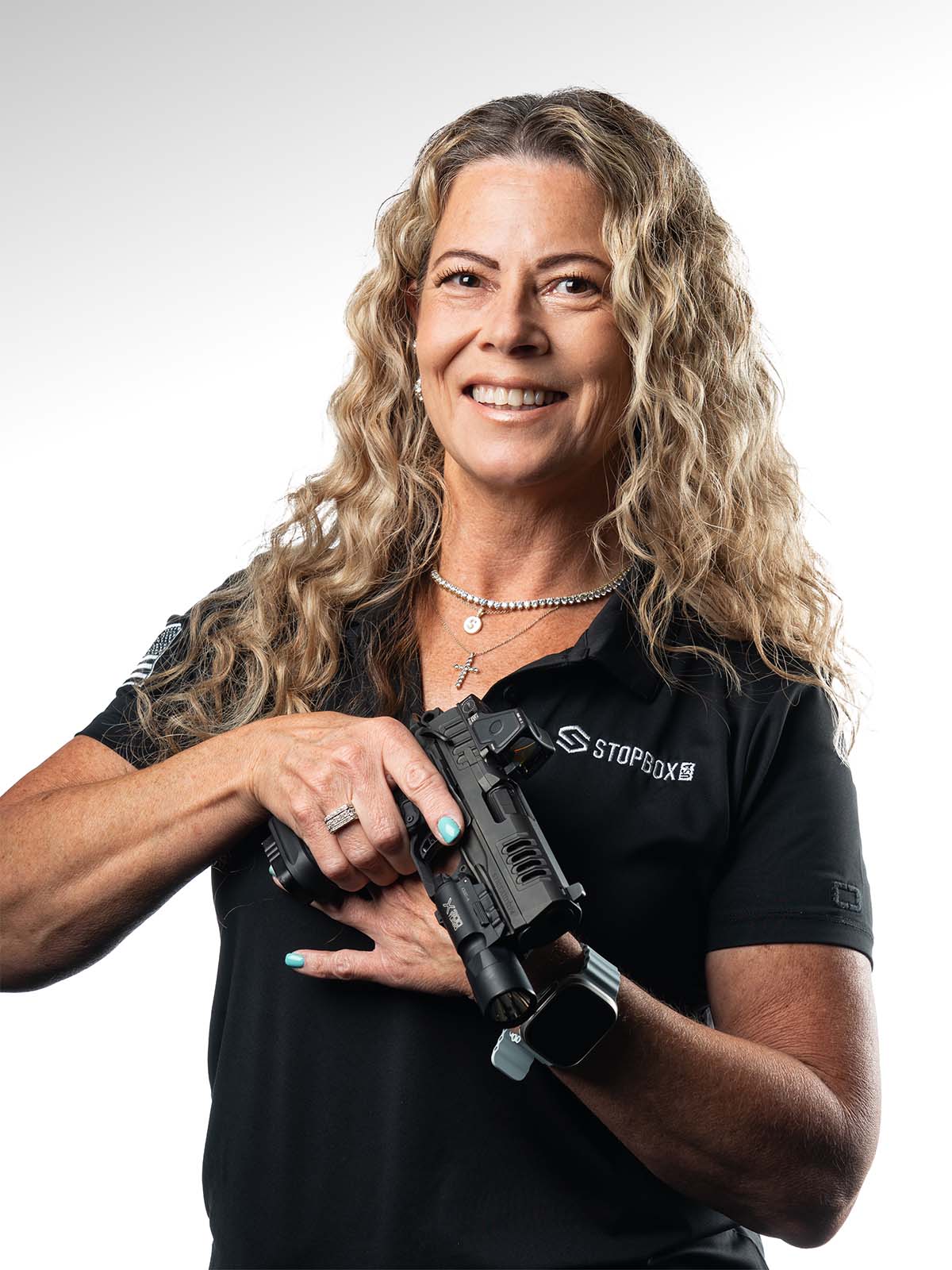 Smiling person holding a firearm with both hands, wearing a black polo shirt.