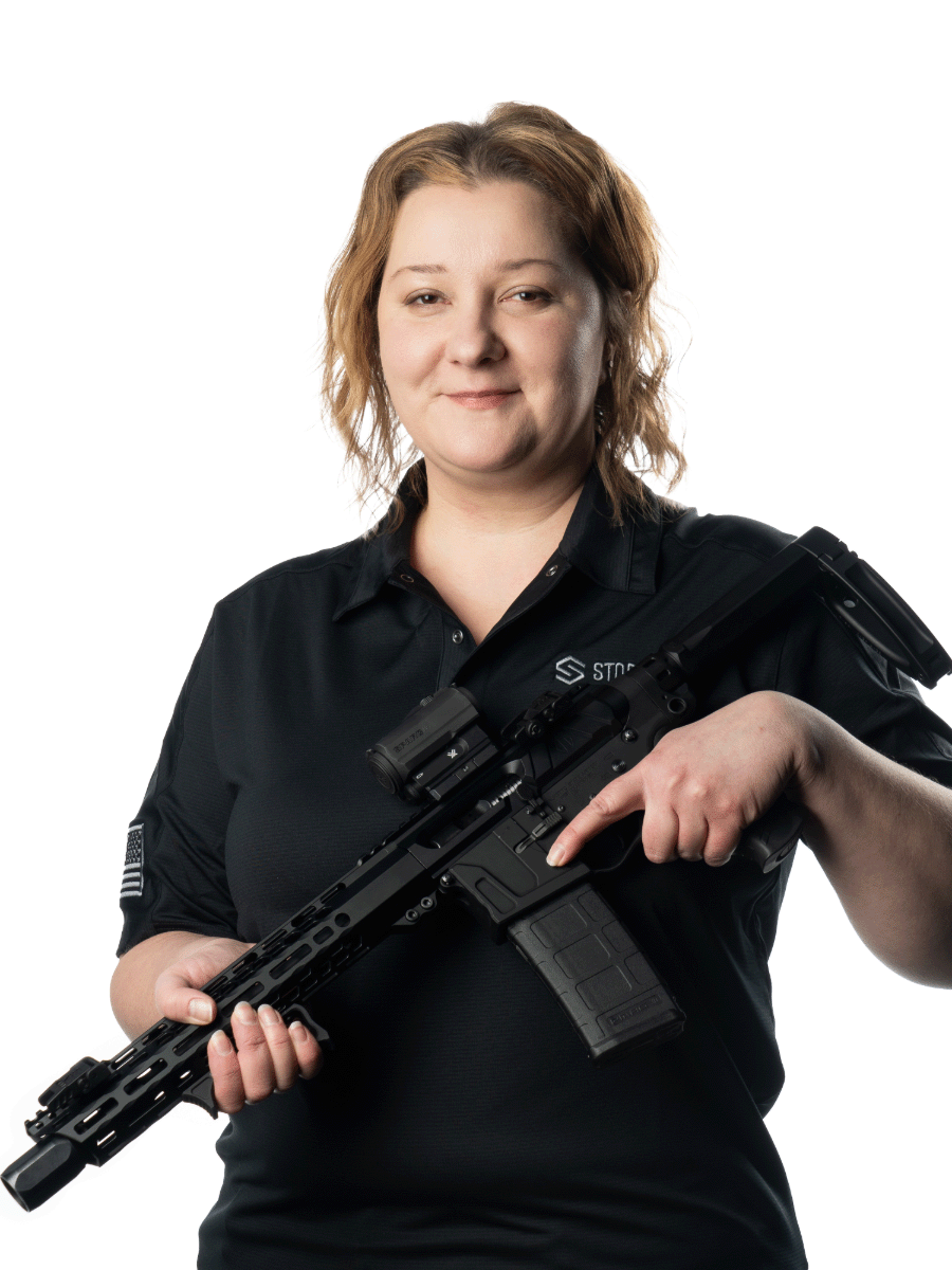 Person holding a rifle, smiling at the camera, wearing a black shirt with a logo.