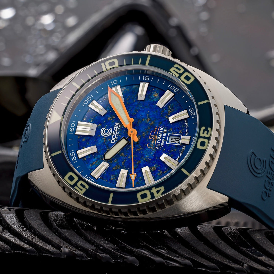An Ocean Crawler watch with a speckled blue dial, orange hands, and a blue rubber strap.