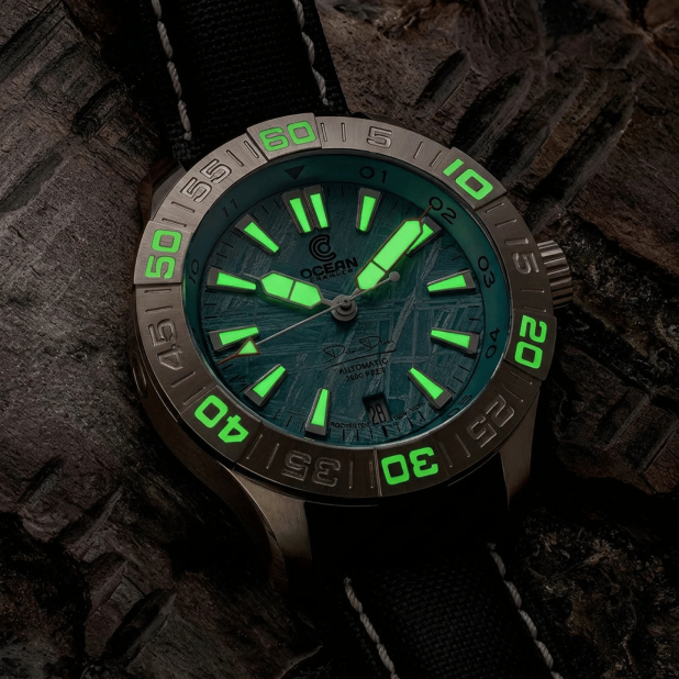 A close-up of a wristwatch with a teal, patterned dial and glowing green hands and hour markers.