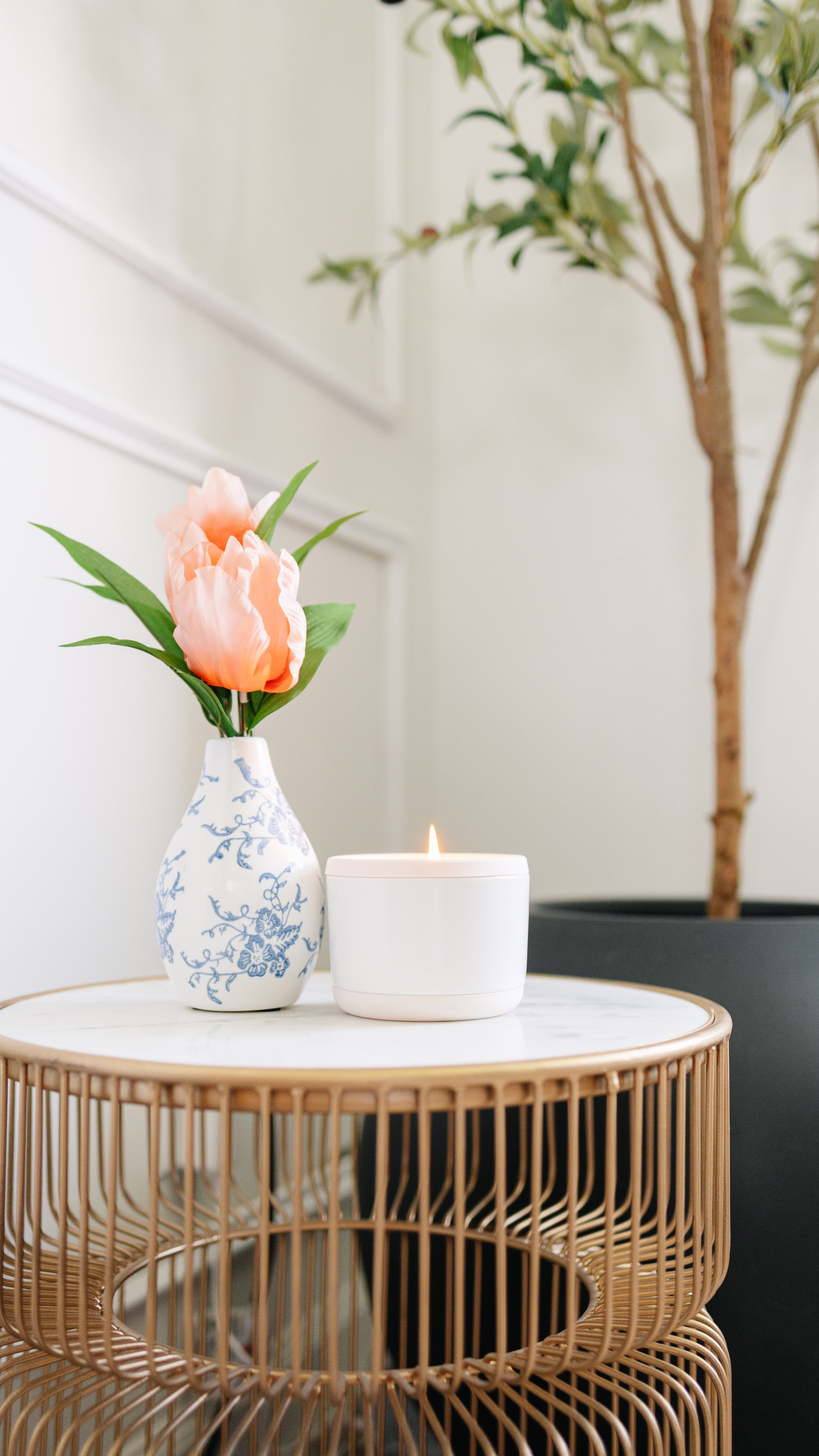 A vase with flowers and a lit candle on a round table.