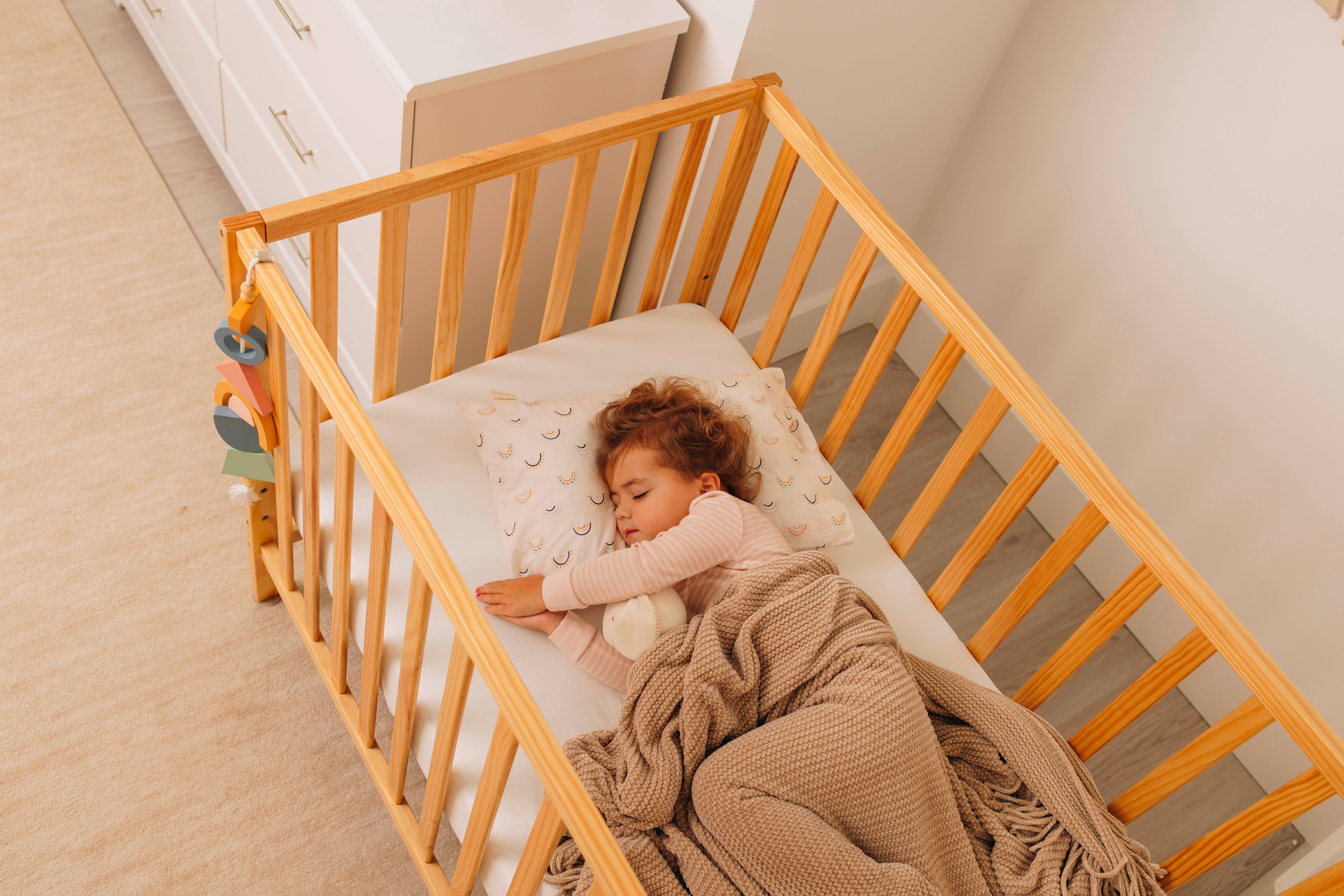 Child sleeping in a wooden crib with a blanket and pillow.