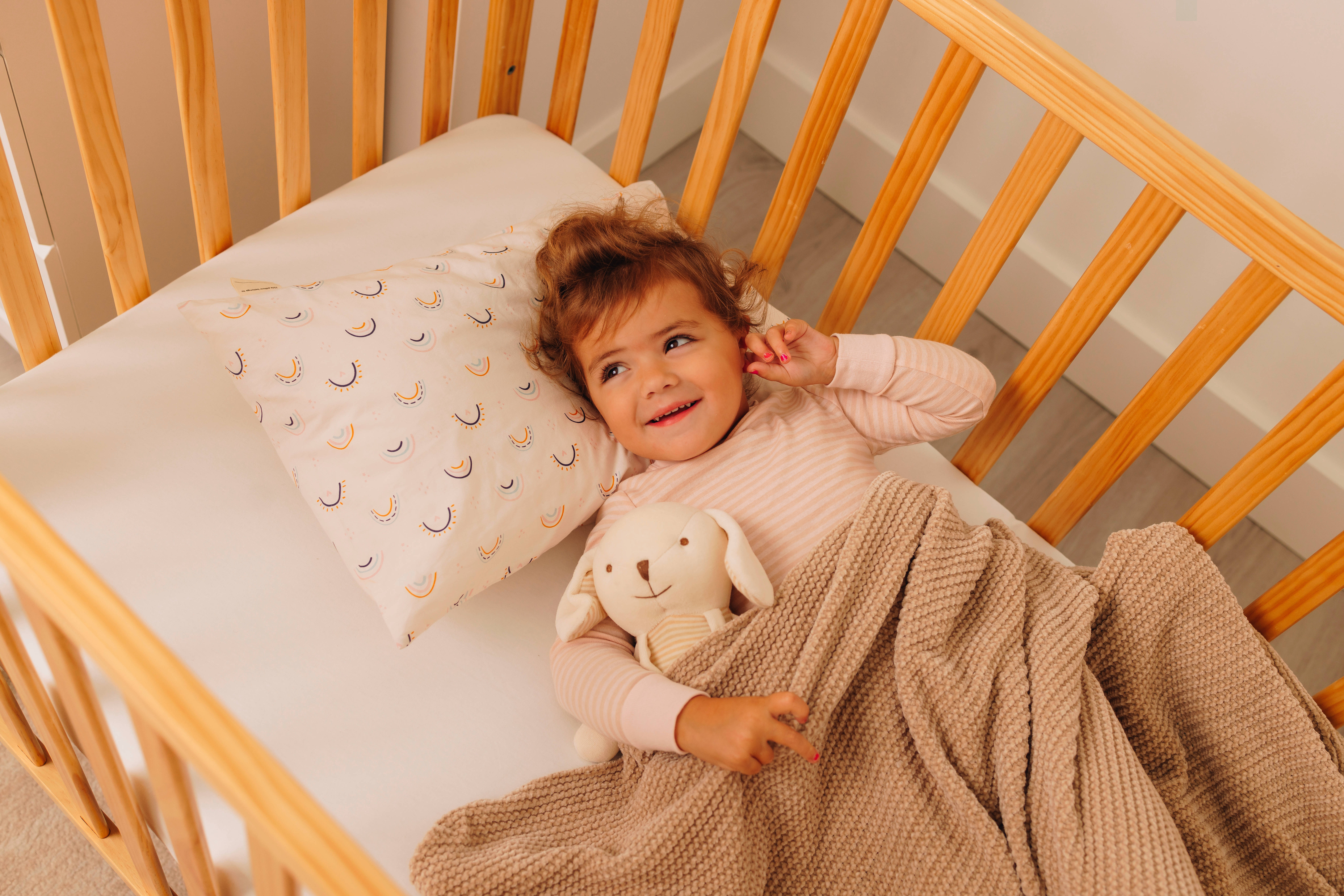 Child lying in a crib with a stuffed toy and blanket.