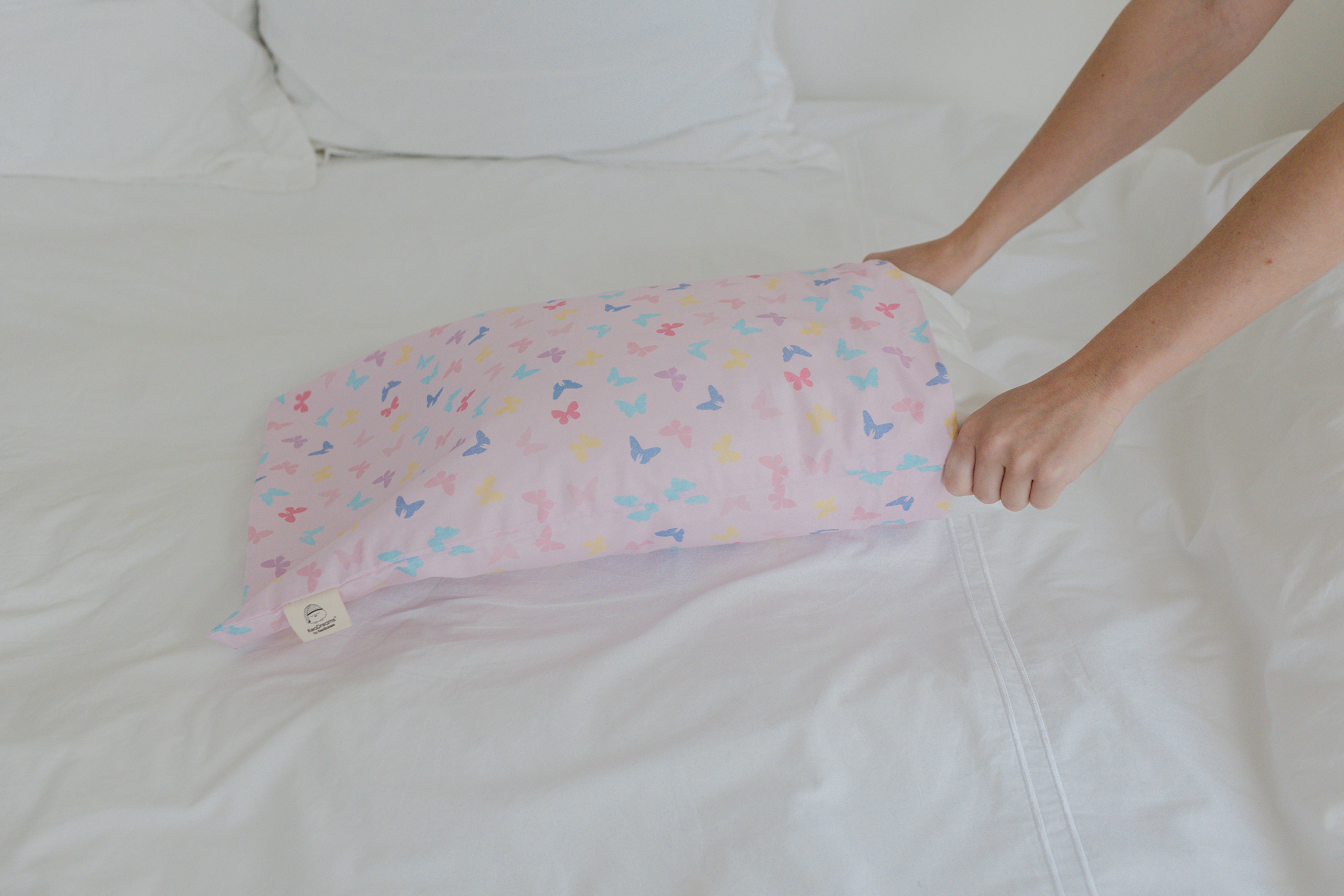 Hands placing a butterfly-patterned pillow on a white bed.