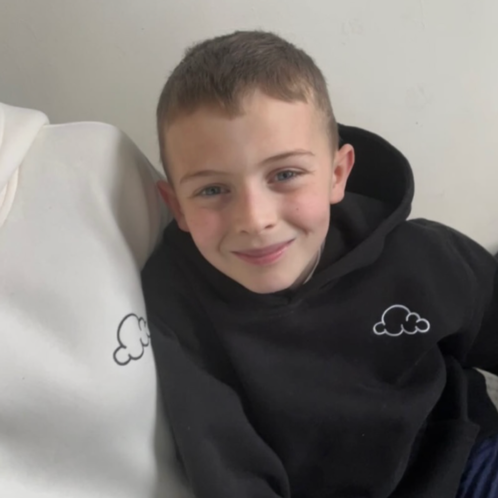 Smiling child in a black hoodie with a cloud design.