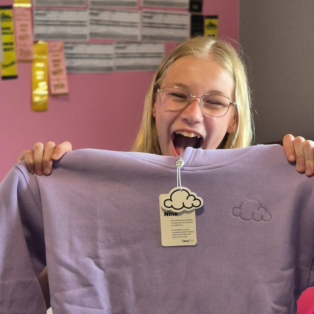 Person excitedly holding a purple sweatshirt with cloud design.