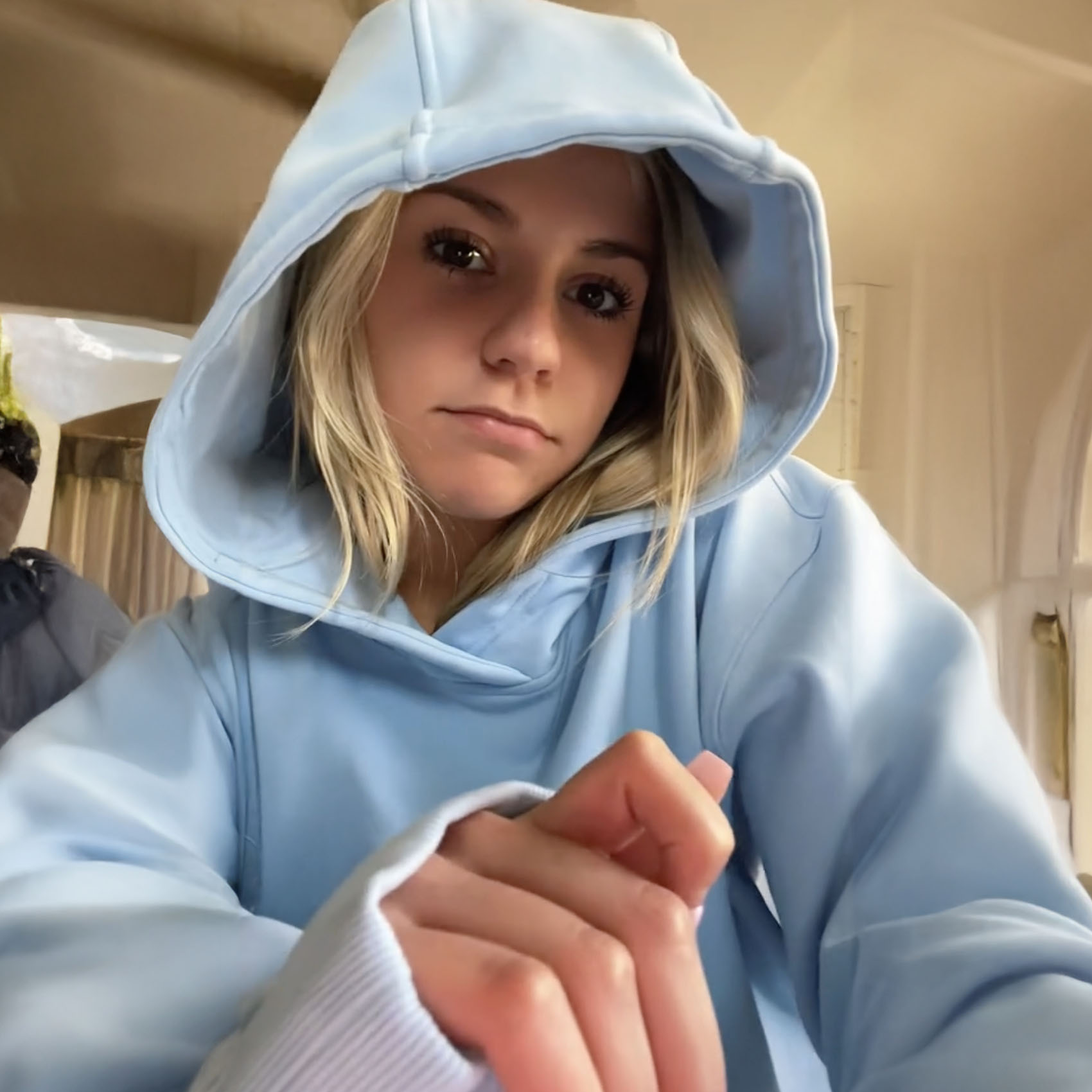 Person in a blue hoodie looking at the camera indoors.