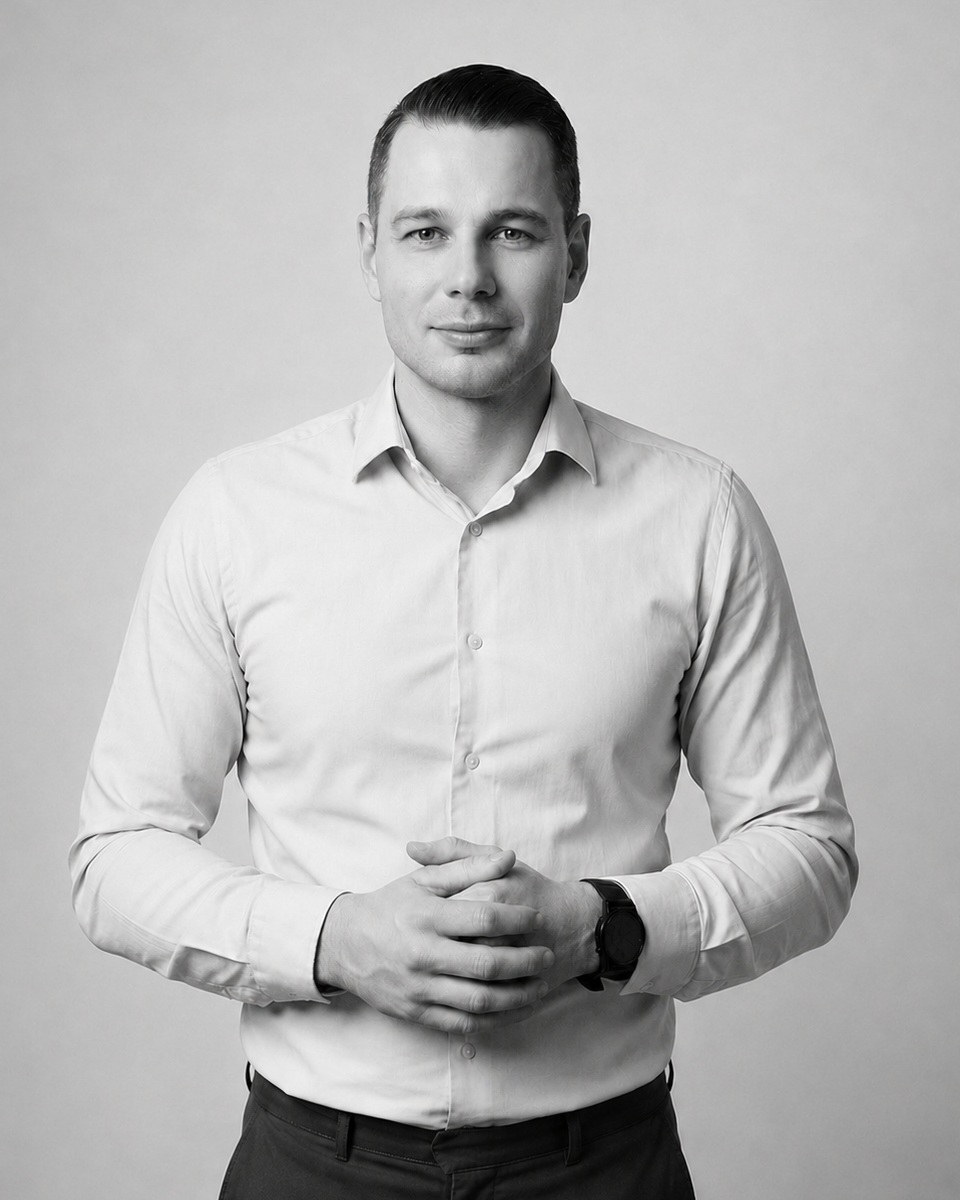 A black and white portrait of a man in a button-down shirt looking directly at the camera.