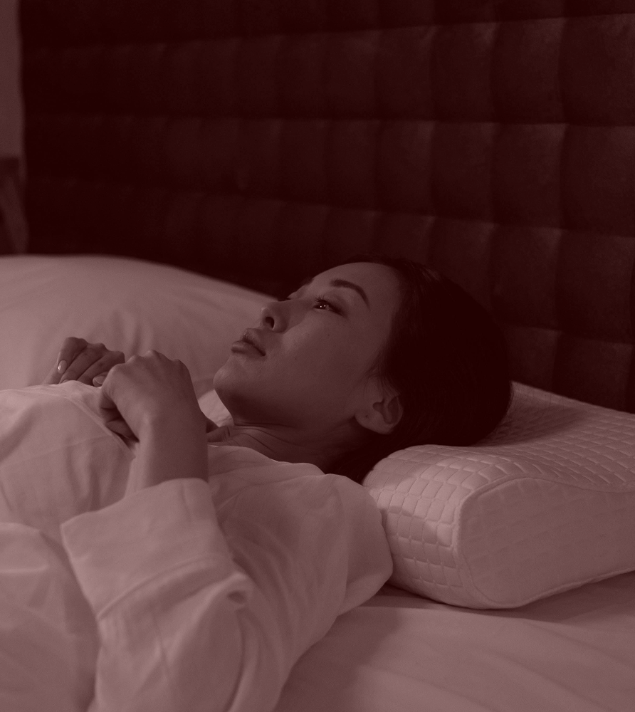 Person lying in bed, looking thoughtful, with a quilted pillow.