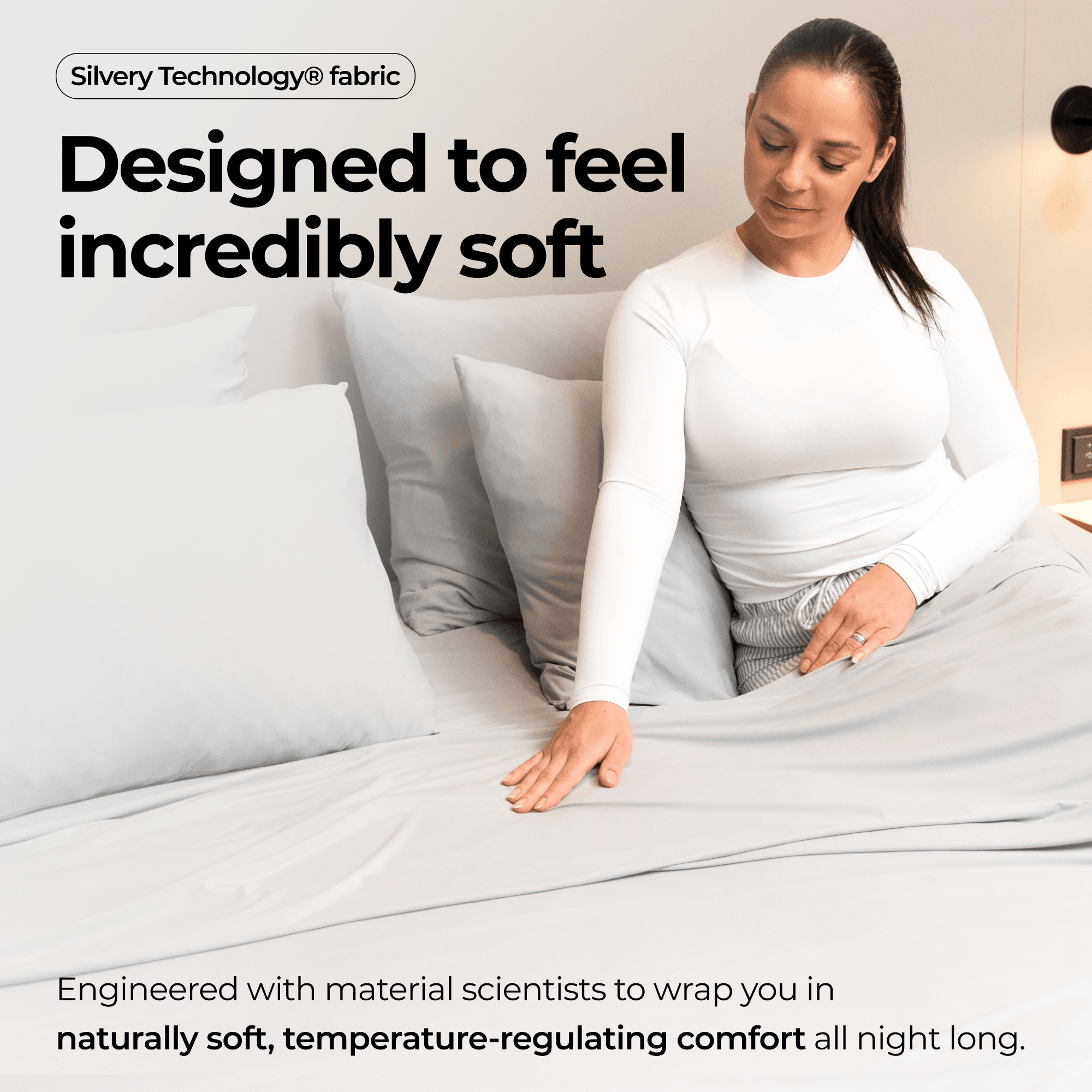A woman in pajamas sits up in bed and touches the soft, light gray sheets.