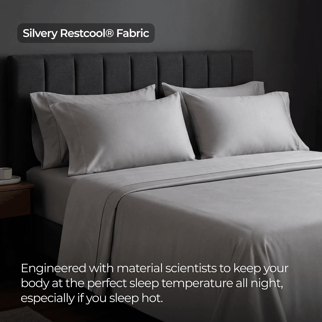 A bed made with silvery gray sheets and pillows against a dark gray, tufted headboard.