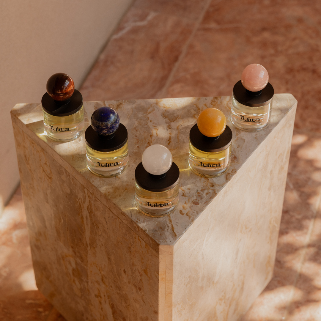 Five perfume bottles with colorful spherical caps on a marble pedestal.