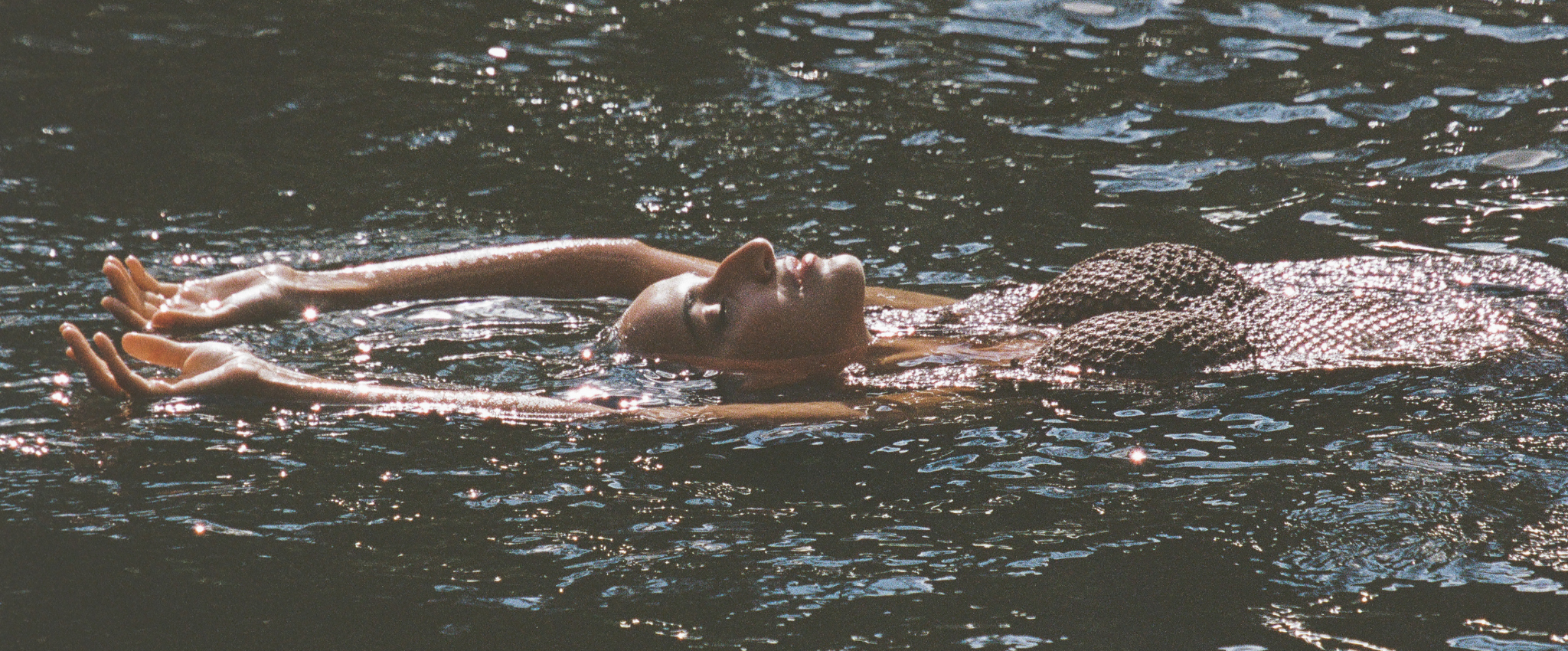 Person floating on water with arms outstretched, wearing a textured top.