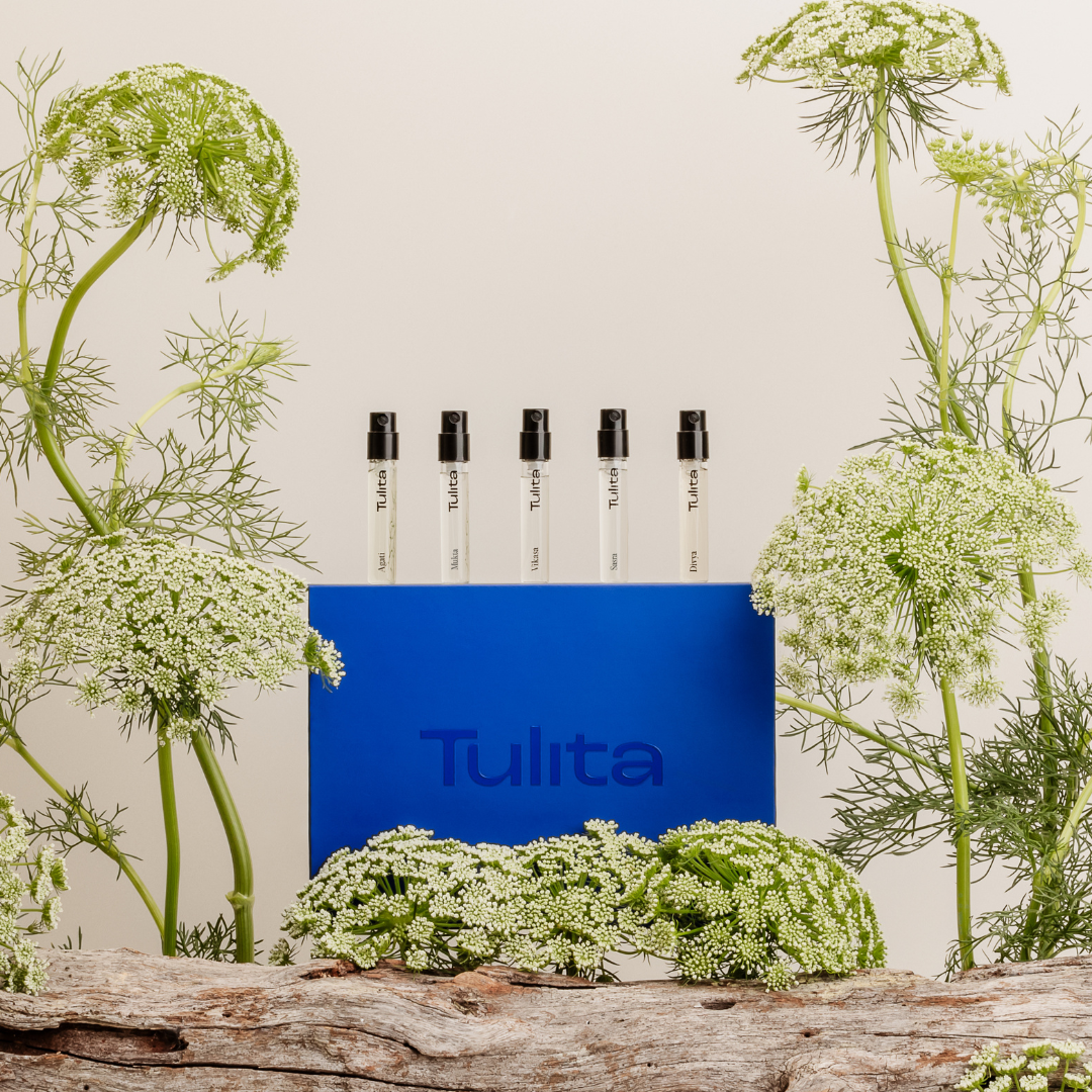 Five perfume bottles on a blue box surrounded by white flowers and greenery.