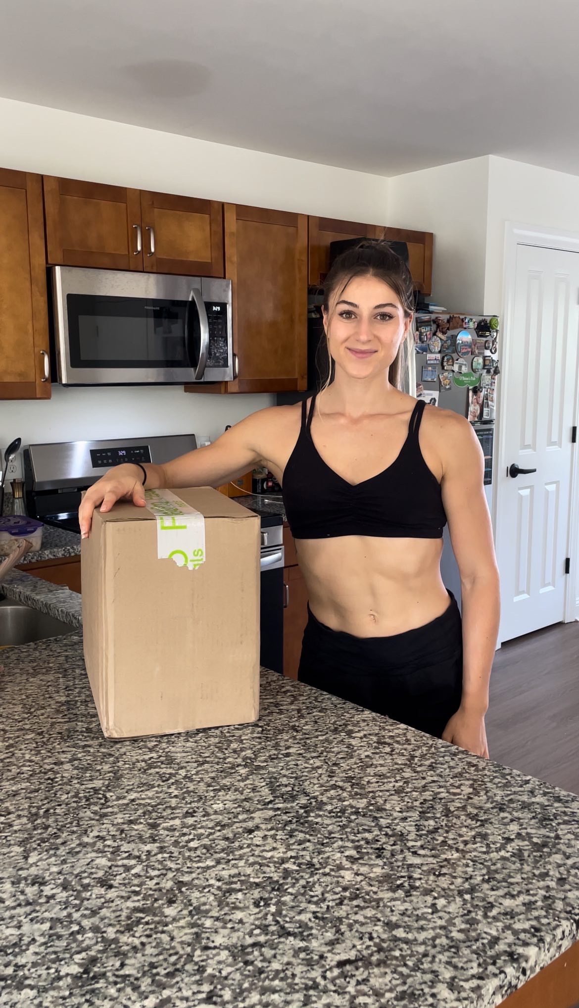 Person in a kitchen with a cardboard box on the counter.