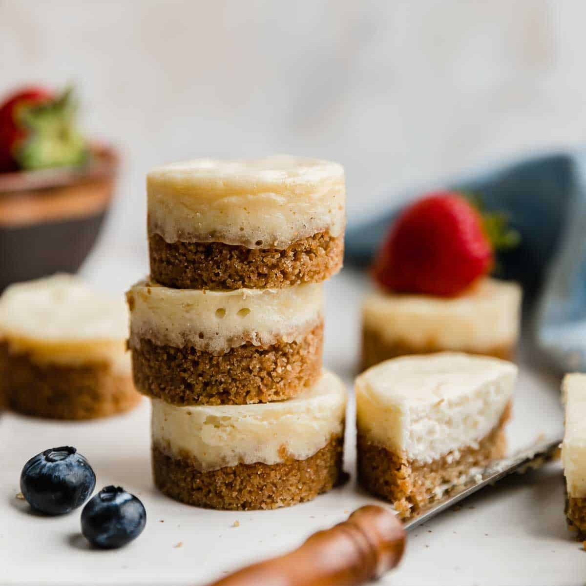 Stack of mini cheesecakes with blueberries and strawberries on a white surface.