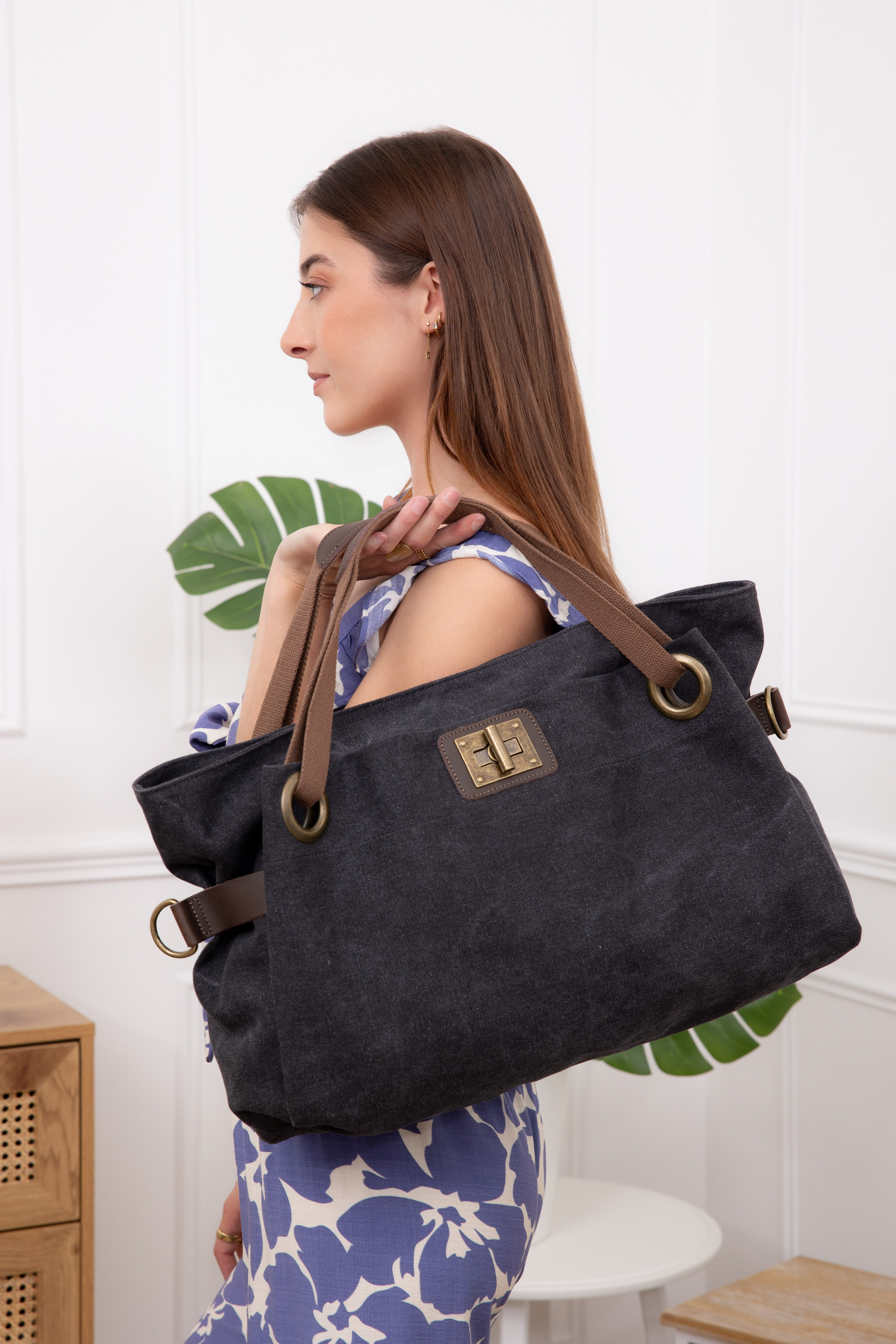 Woman holding a large black handbag with brown straps indoors.