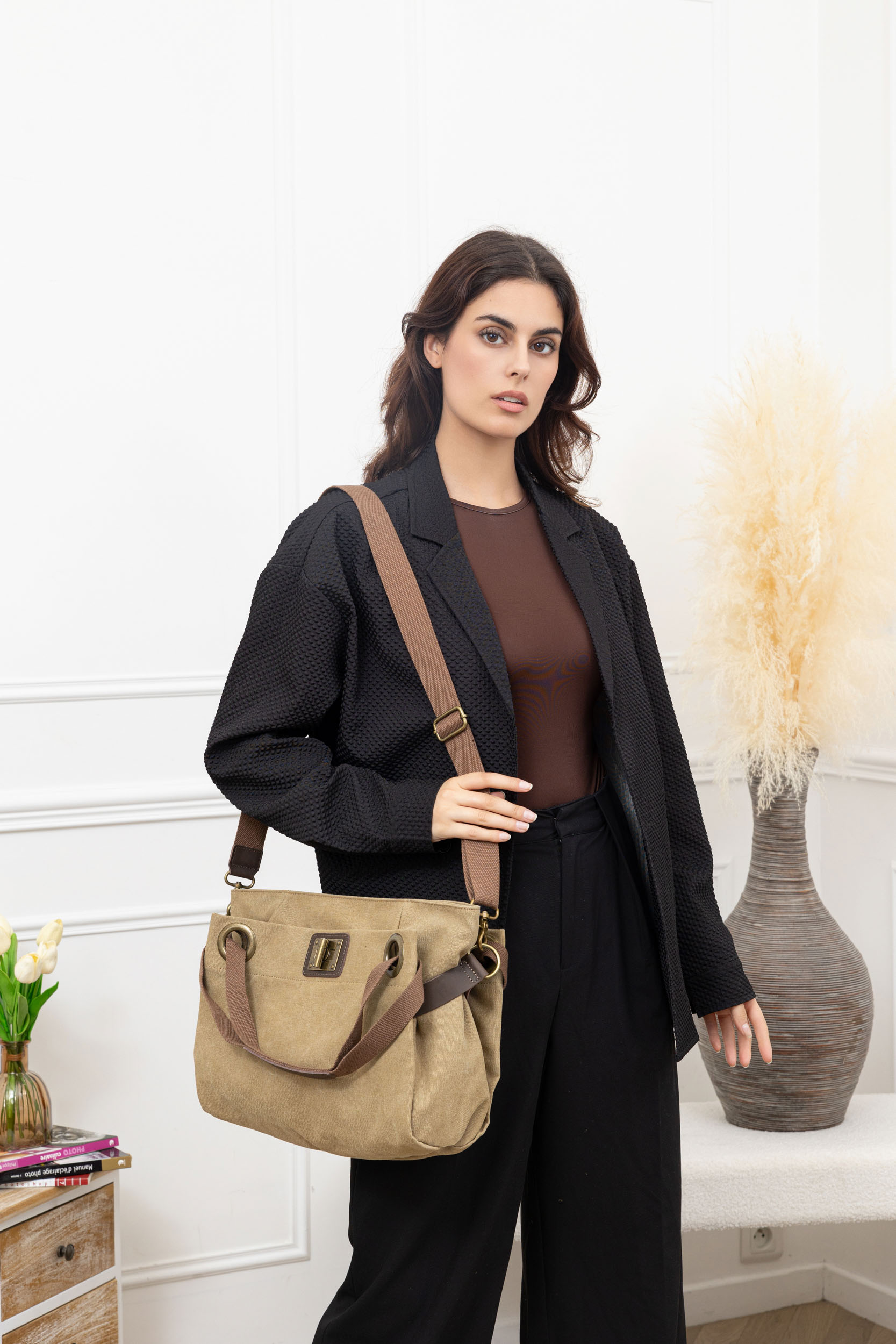 Person in black jacket holding a beige handbag indoors.