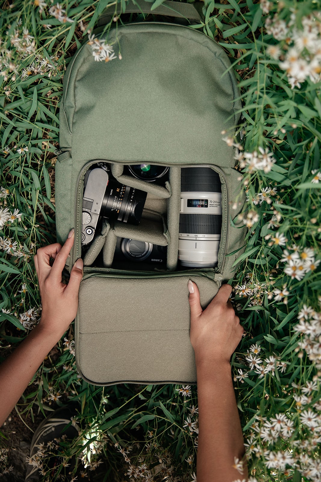 Hands opening a camera bag with lenses among green foliage.
