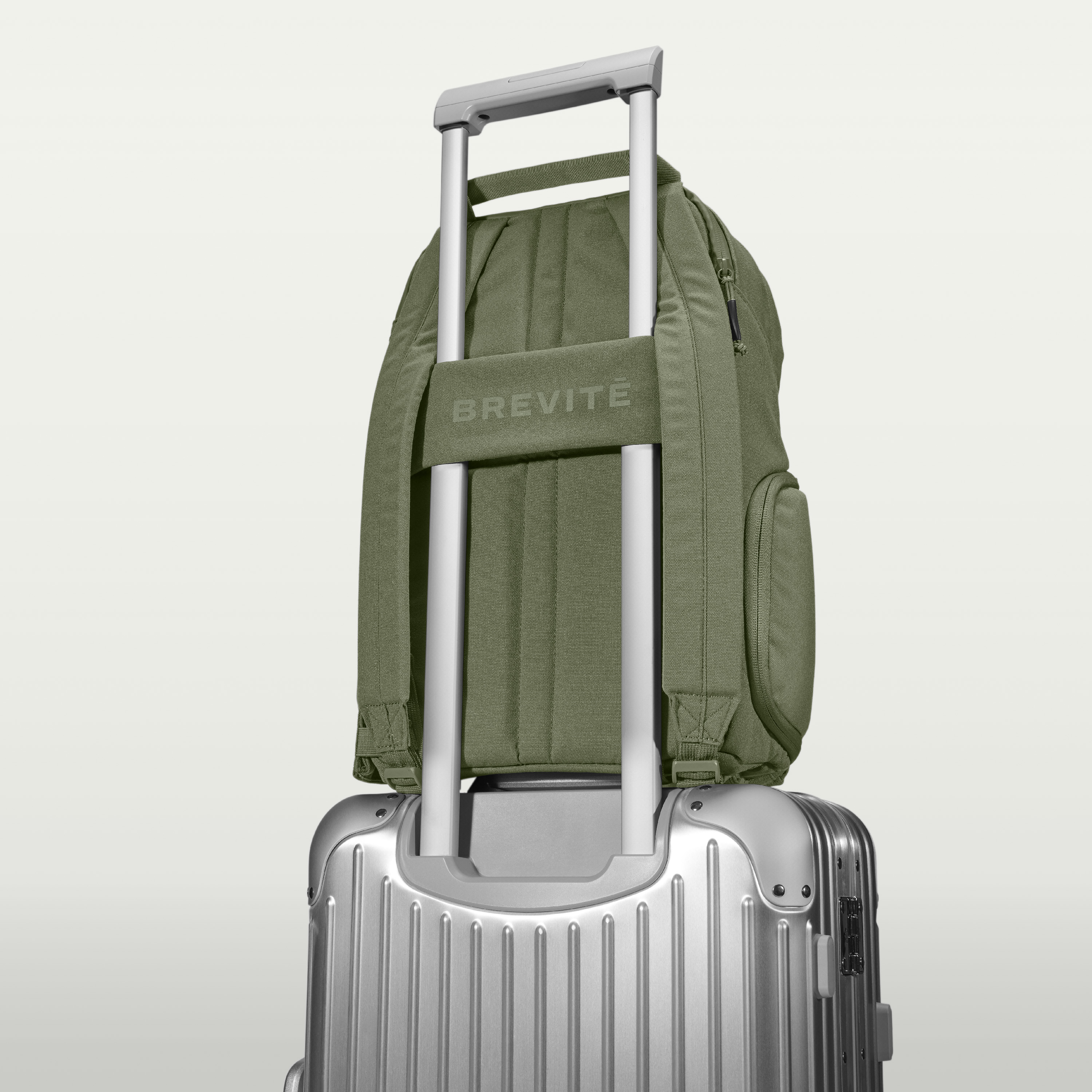 Green backpack attached to a silver suitcase handle.
