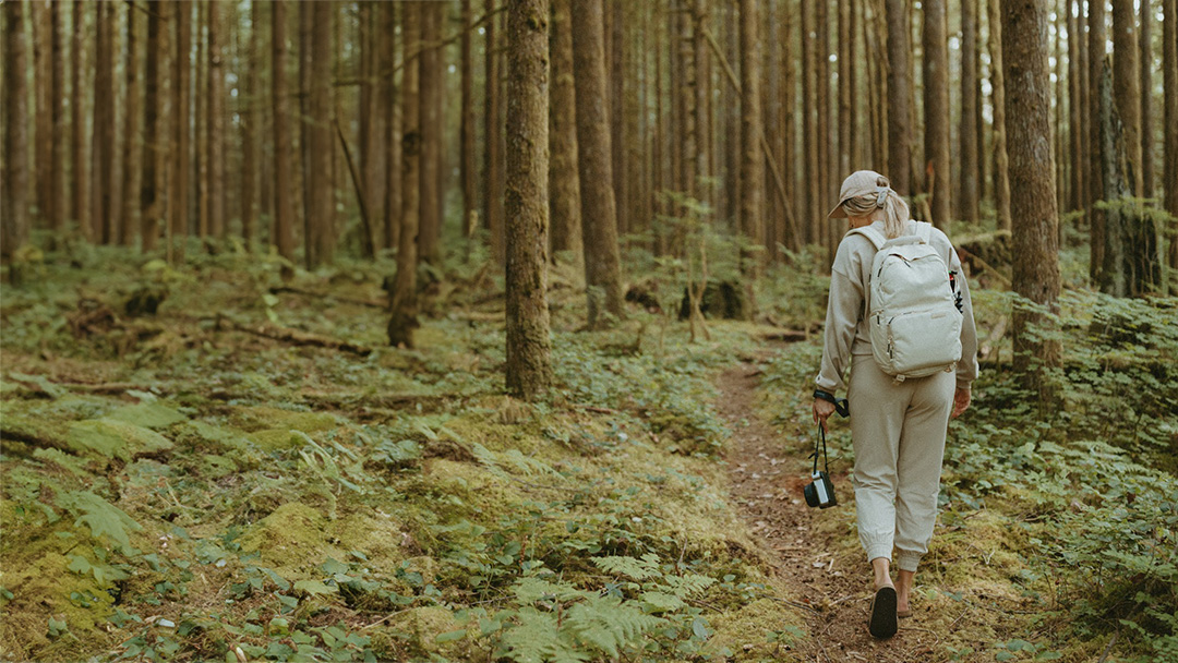 Person with backpack walking through a dense forest trail.