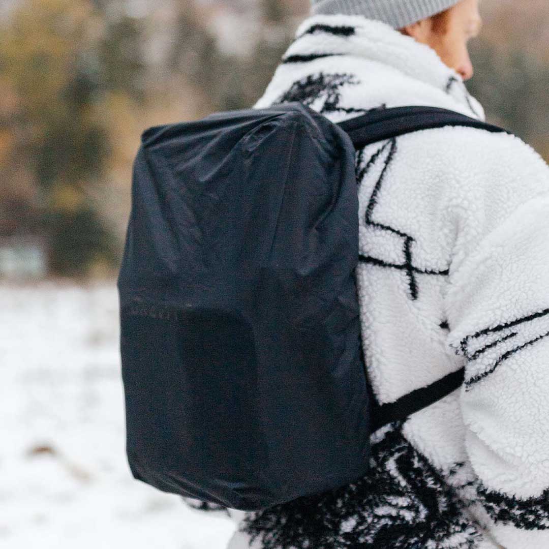 Person wearing a black backpack and white patterned jacket outdoors.