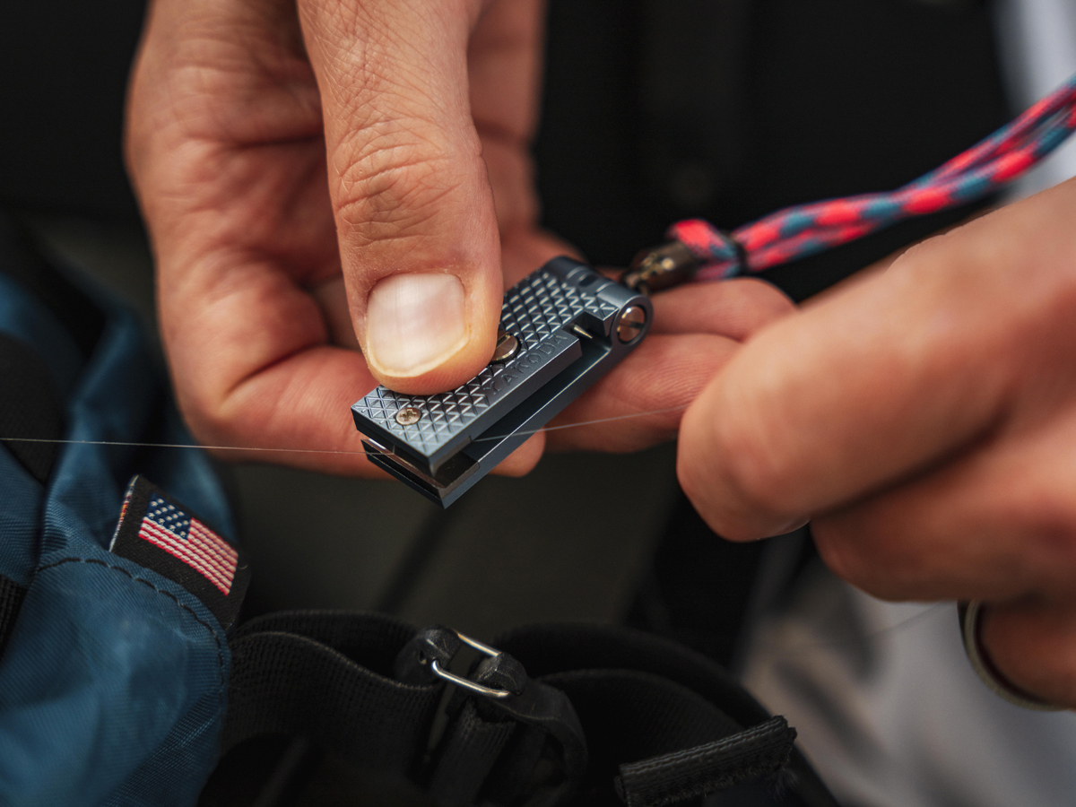 Person holding a metal tool with a lanyard, near a blue bag with a flag patch.